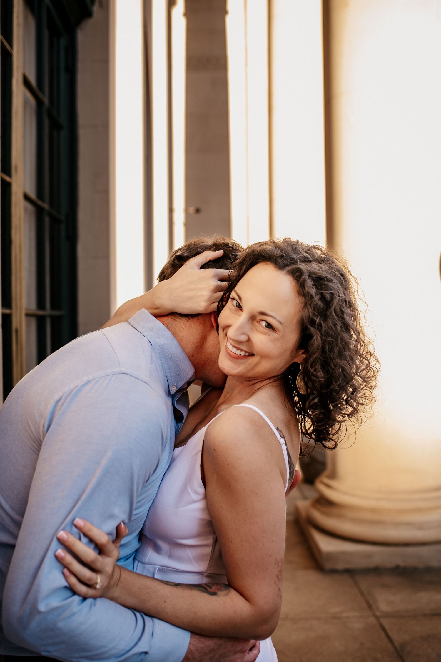 Romantic couple embracing and laughing in front of classical columns during golden hour.