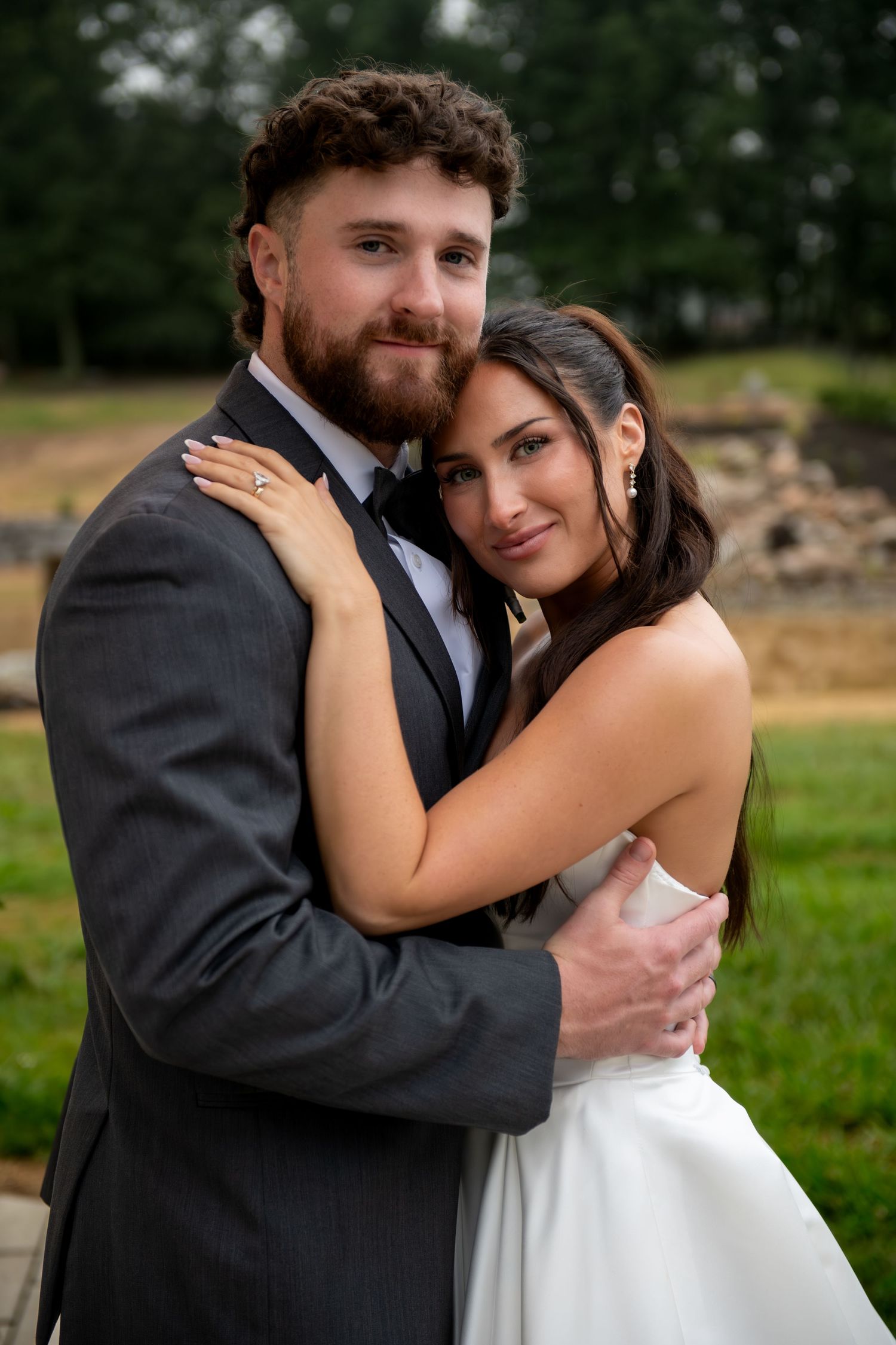 Bride and groom embracing outdoors, wearing wedding attire, sharing a romantic moment on their wedding day.