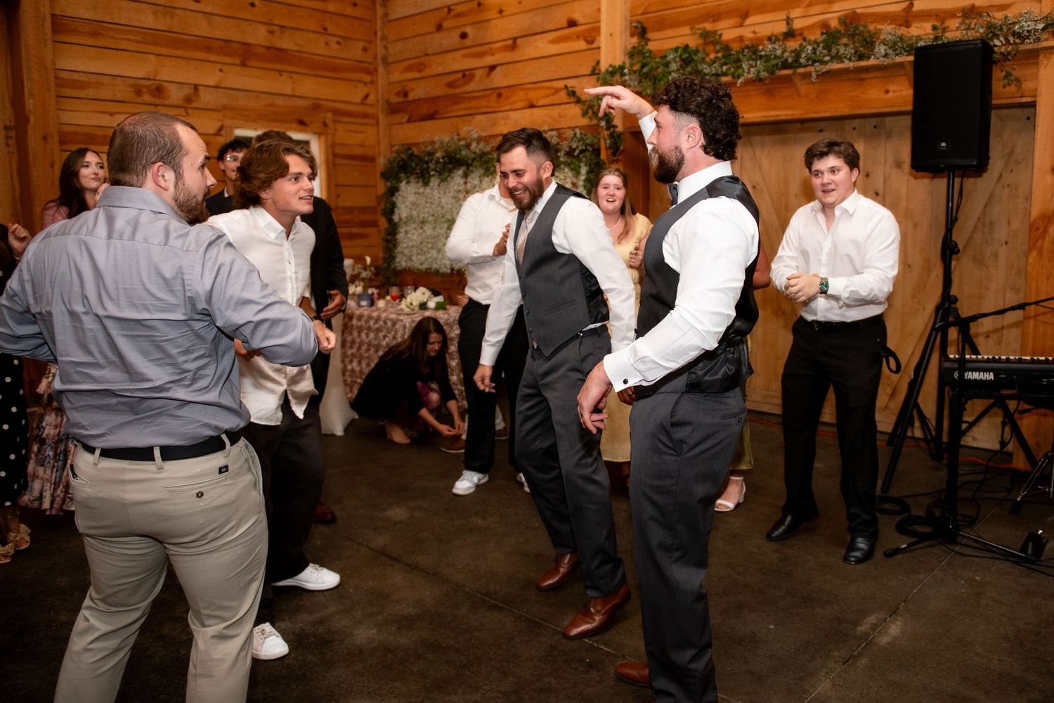 Guests dancing energetically at a rustic barn wedding reception with wood-paneled walls and string lights.