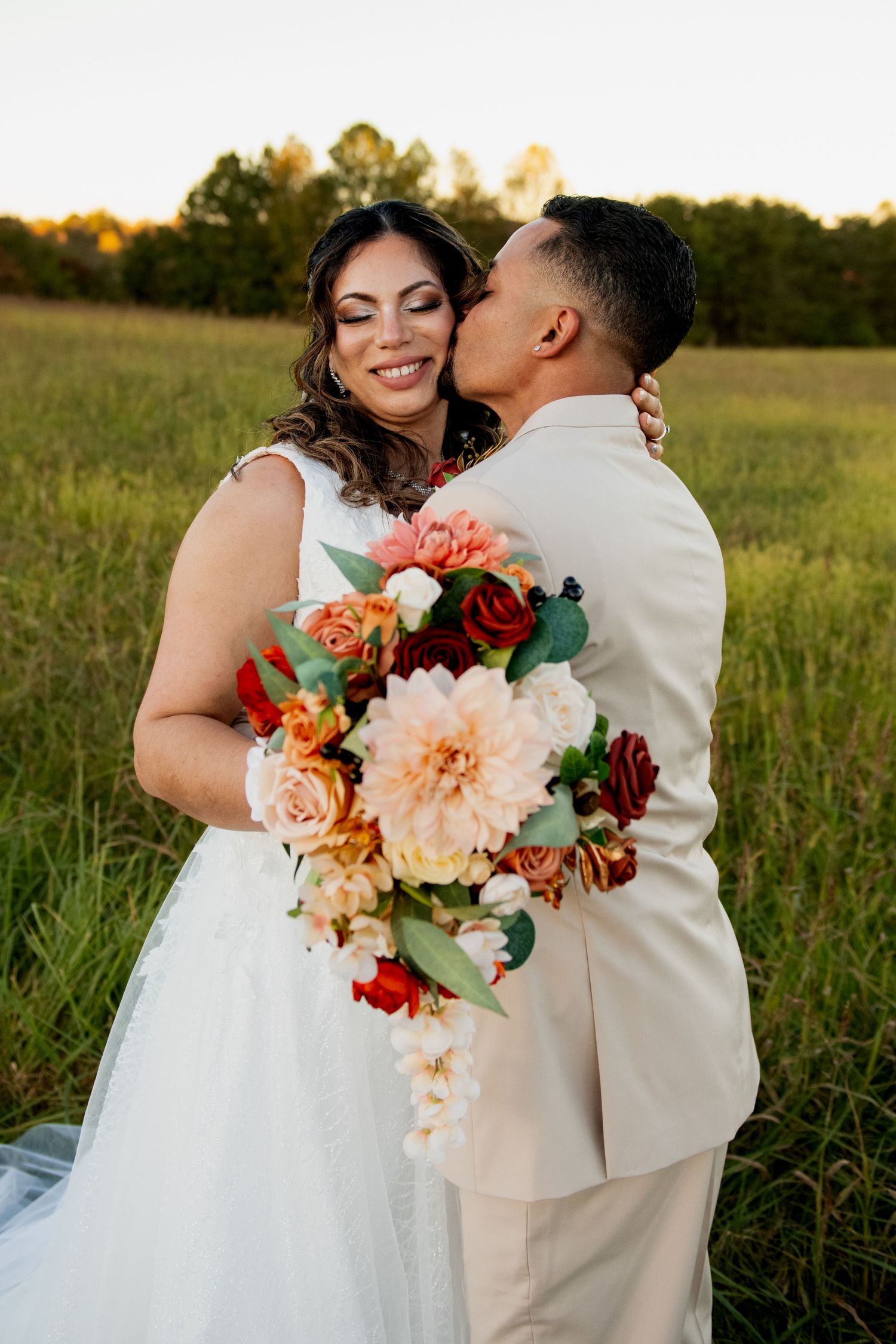 A tender wedding moment captured in a field at sunset with a stunning coral and peach floral bouquet.