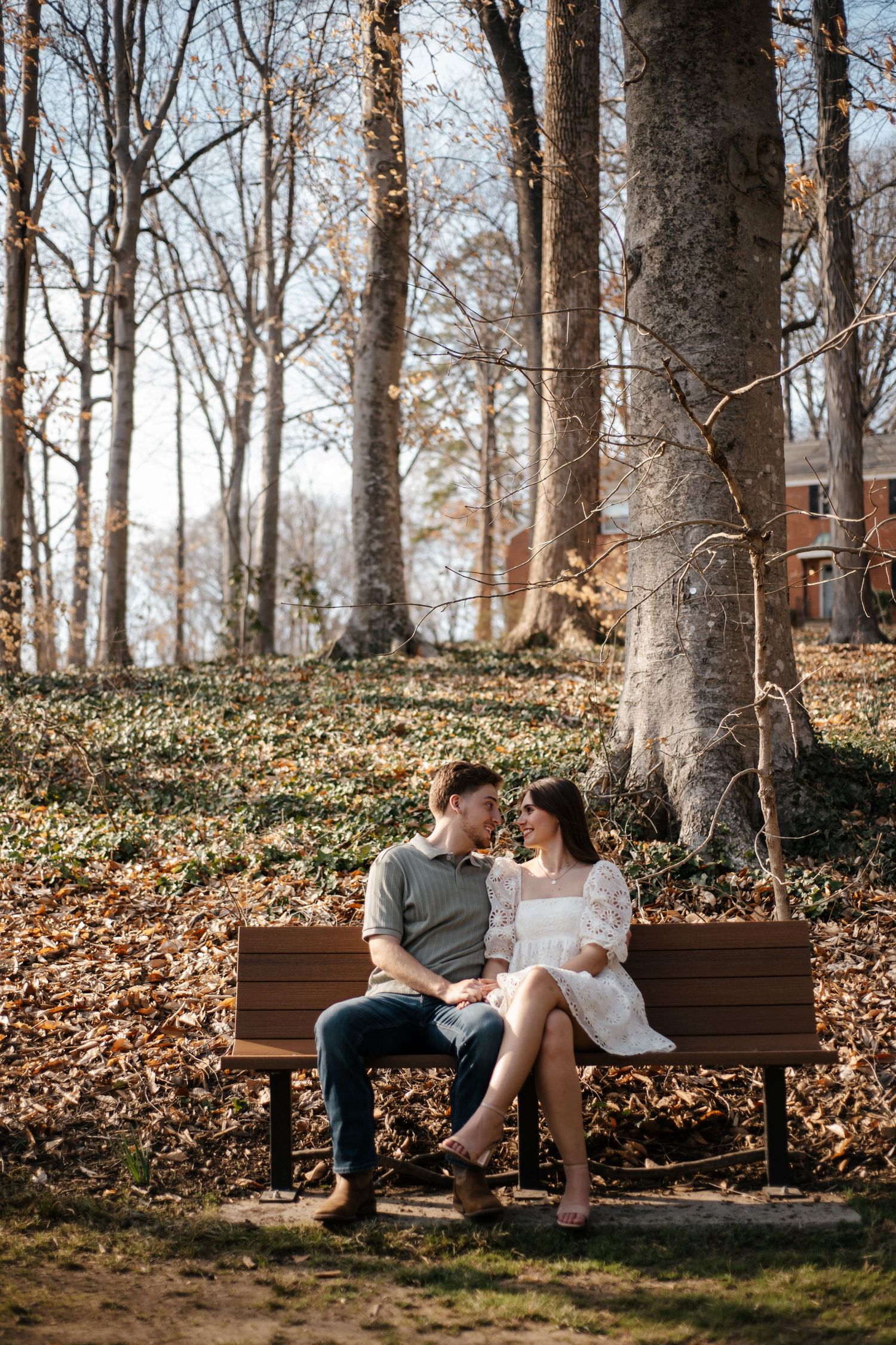 A couple shares an intimate moment while sitting on a wooden bench in a wooded park.