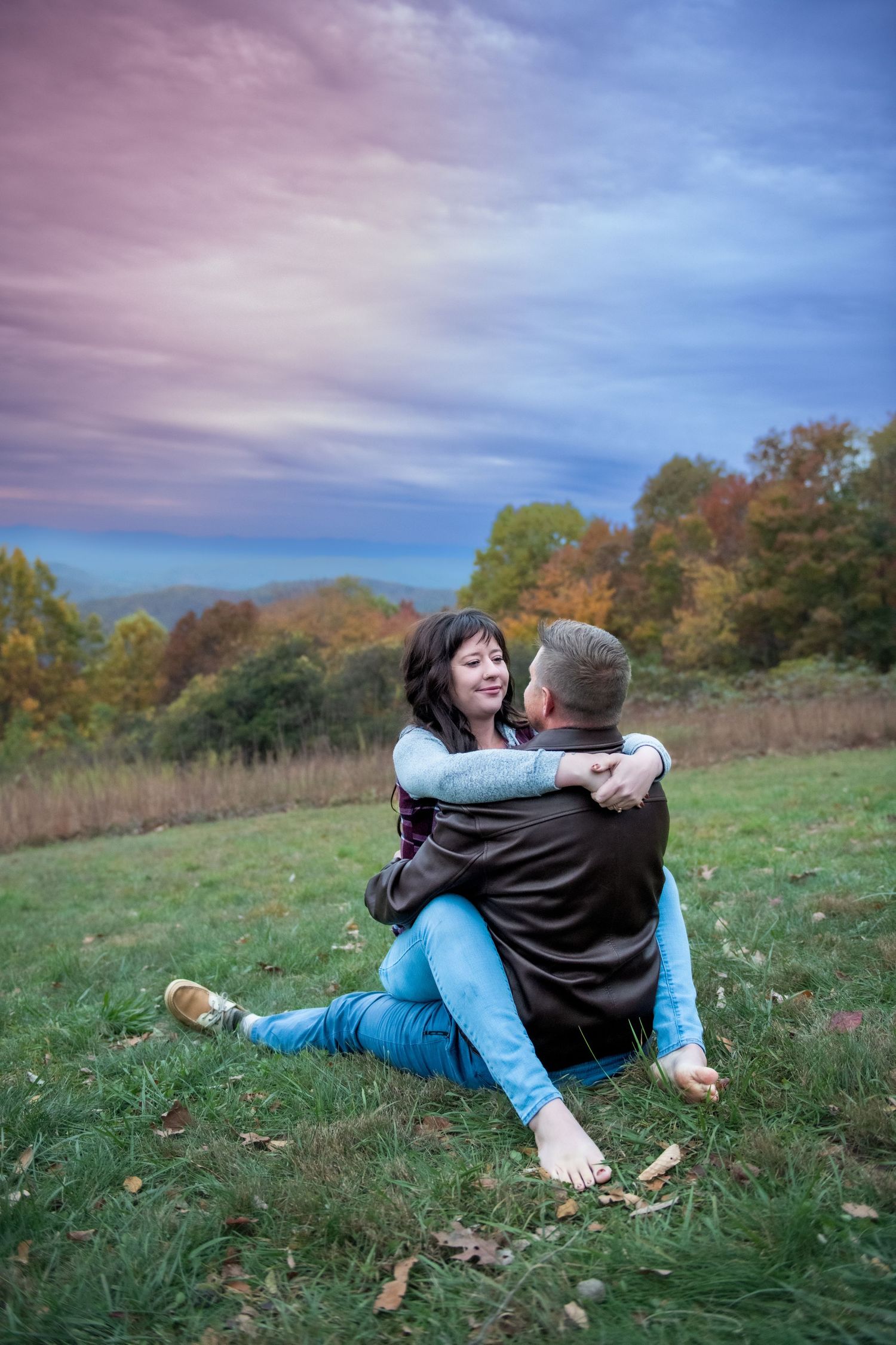 A couple shares a tender moment while lying in a grassy autumn field during sunset.