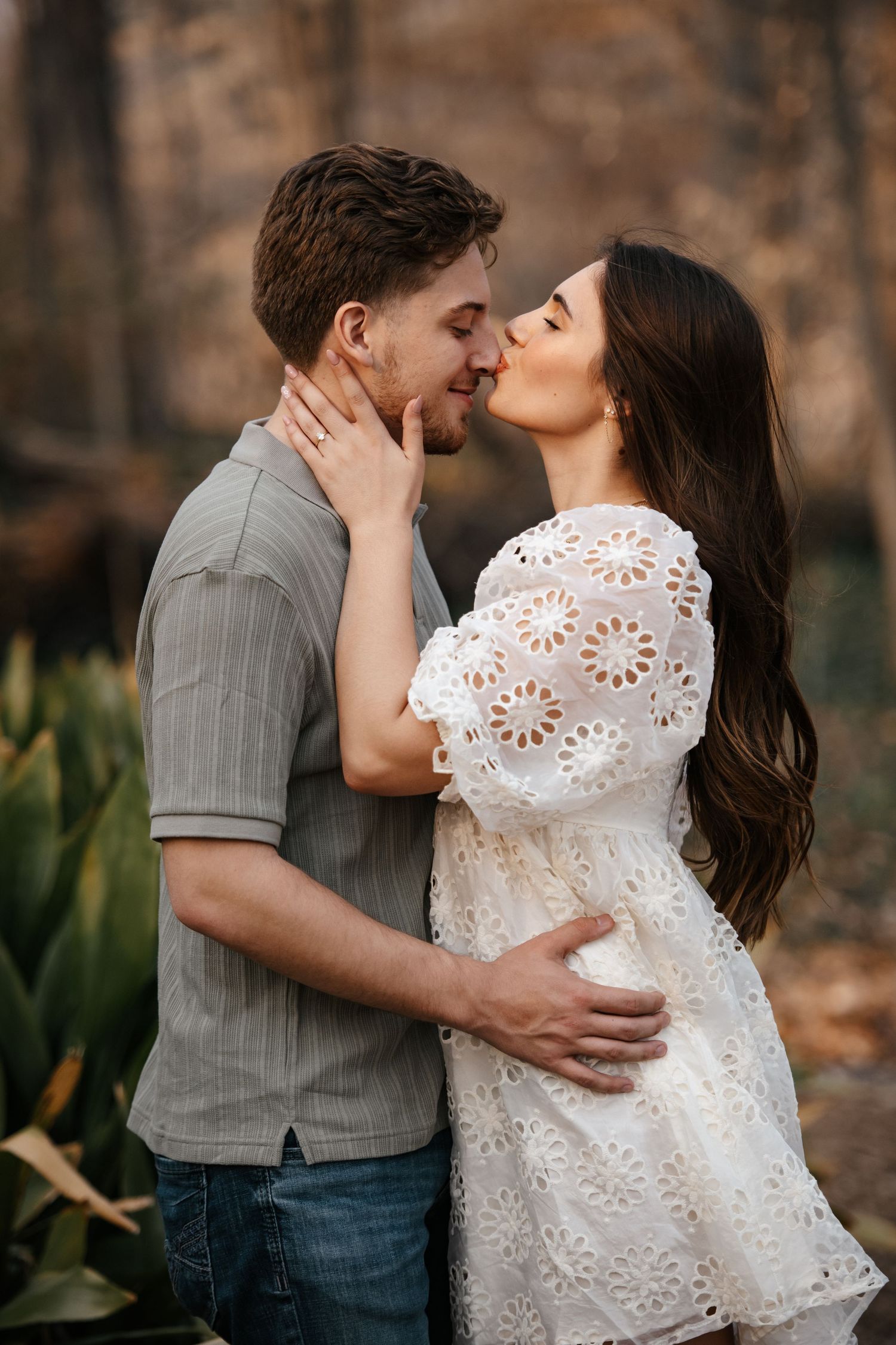 A couple shares an intimate kiss in a garden setting with soft natural lighting.