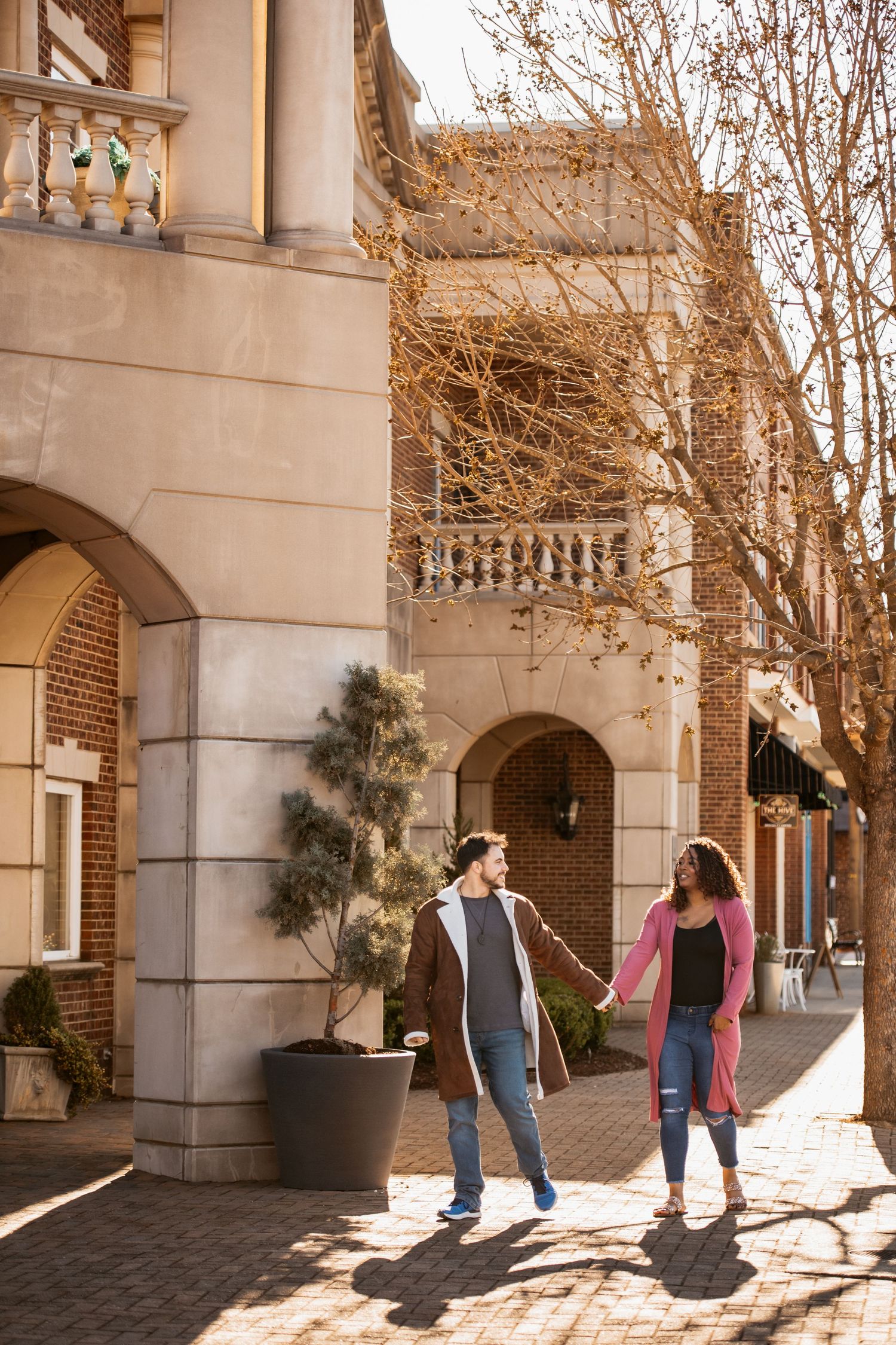 Playful couple walking and dancing in front of a stone building with arched doorways.