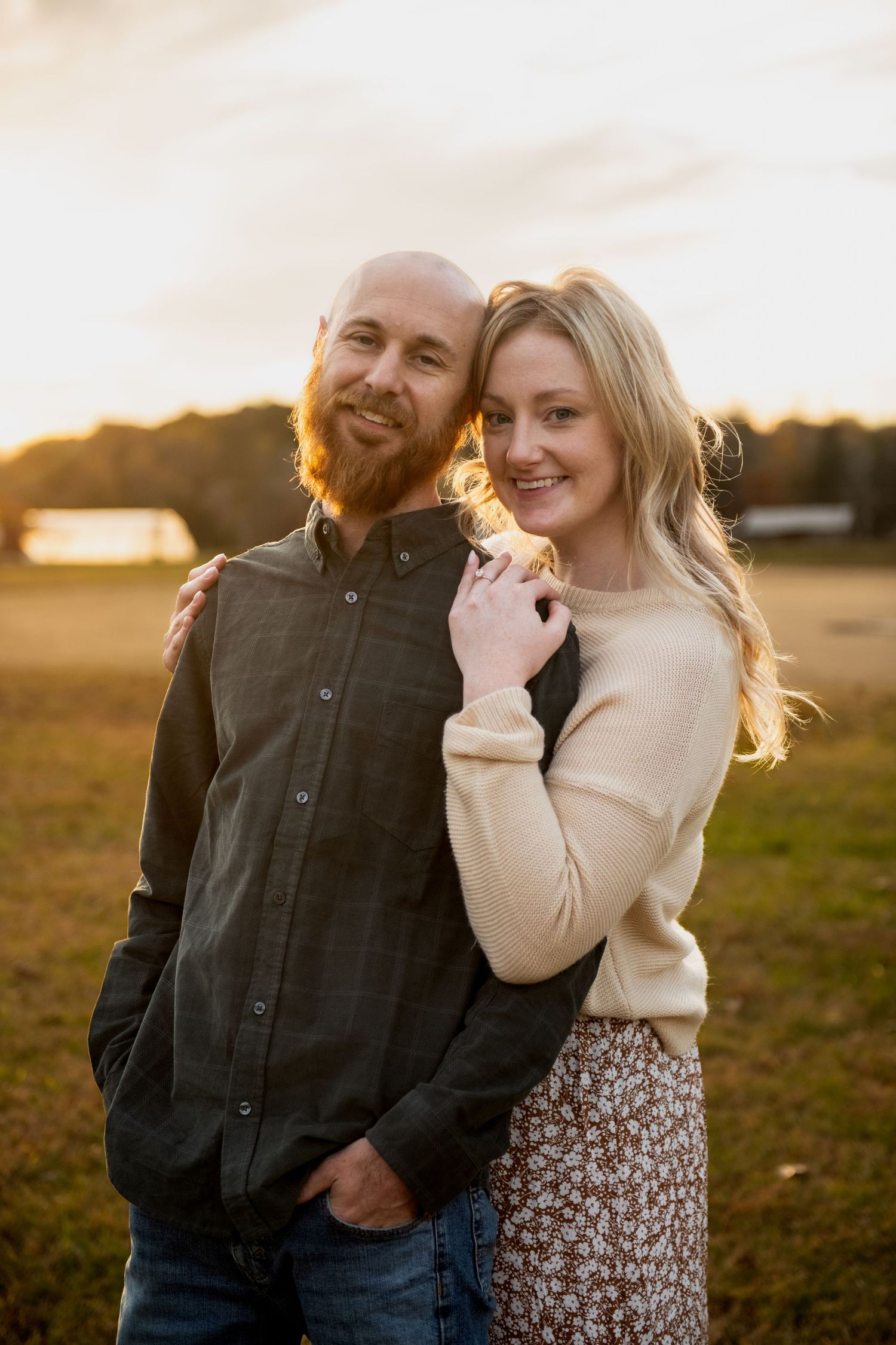 Couple sharing intimate moments in a golden field during sunset while wearing casual autumn attire.