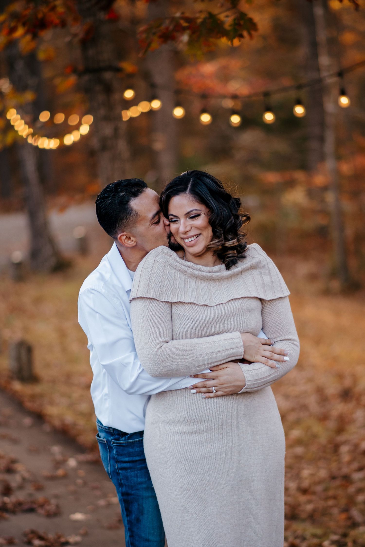 Couple embracing in a warm autumn setting with bokeh lights in background.