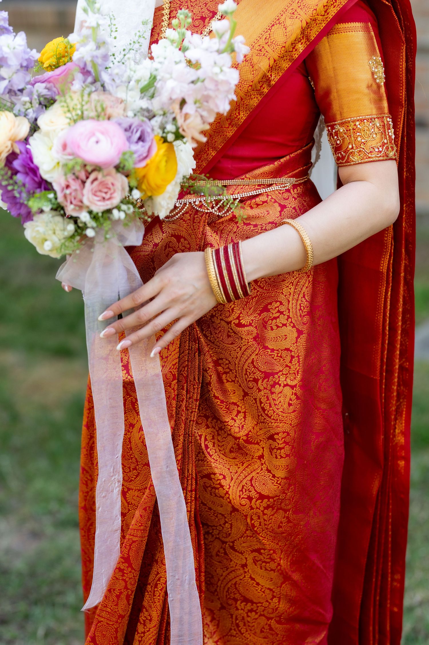 Close-up of traditional red and gold Indian wedding sari with floral bouquet.