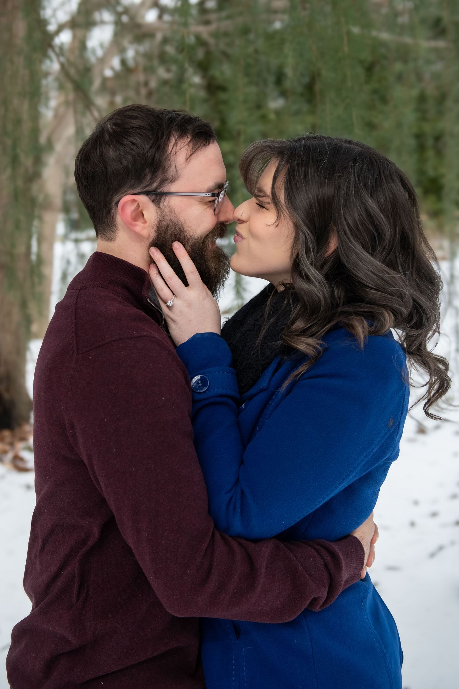 A romantic winter moment between two people in blue and burgundy sweaters embracing in the snow.