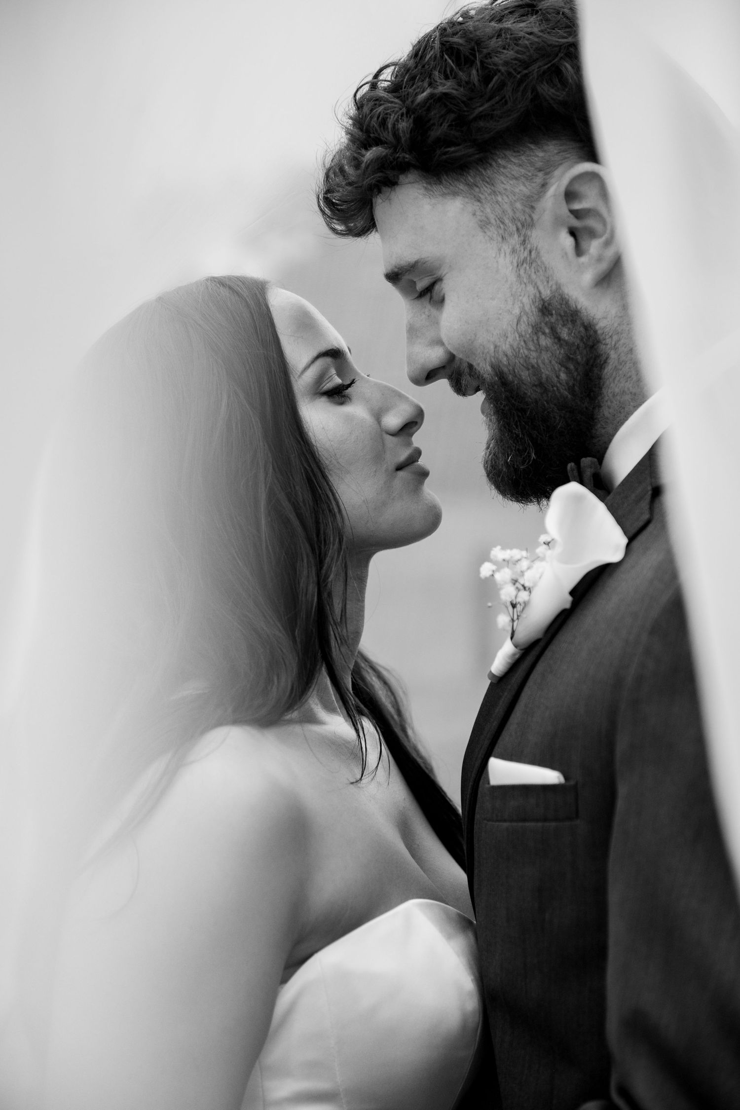 Black and white wedding portrait of bride and groom sharing a romantic moment, veil draped softly around them.