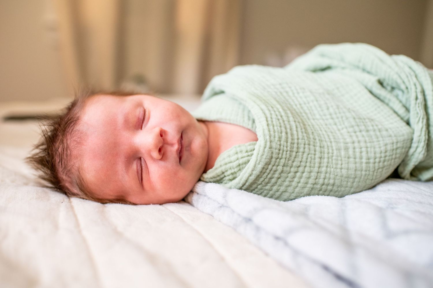 A sleeping newborn baby in soft green clothing rests peacefully on white bedding.