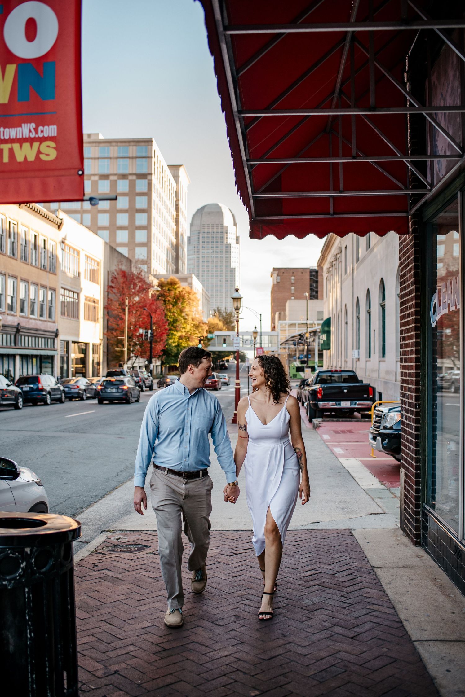 Couple walking and laughing together under red awnings in an urban setting.