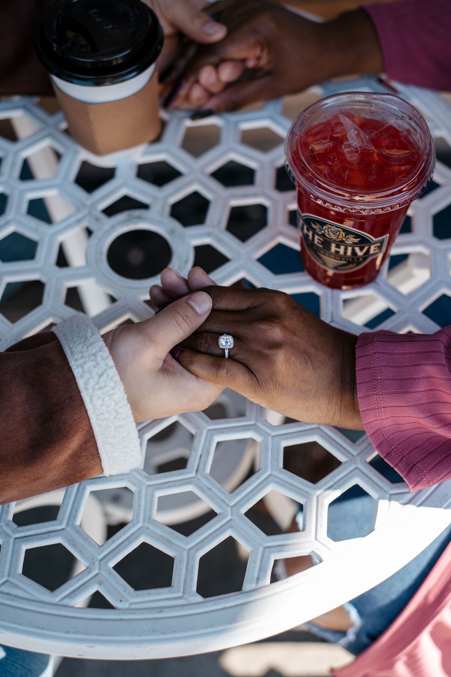 Two hands clasped together on a white geometric patterned table with beverages in the background.