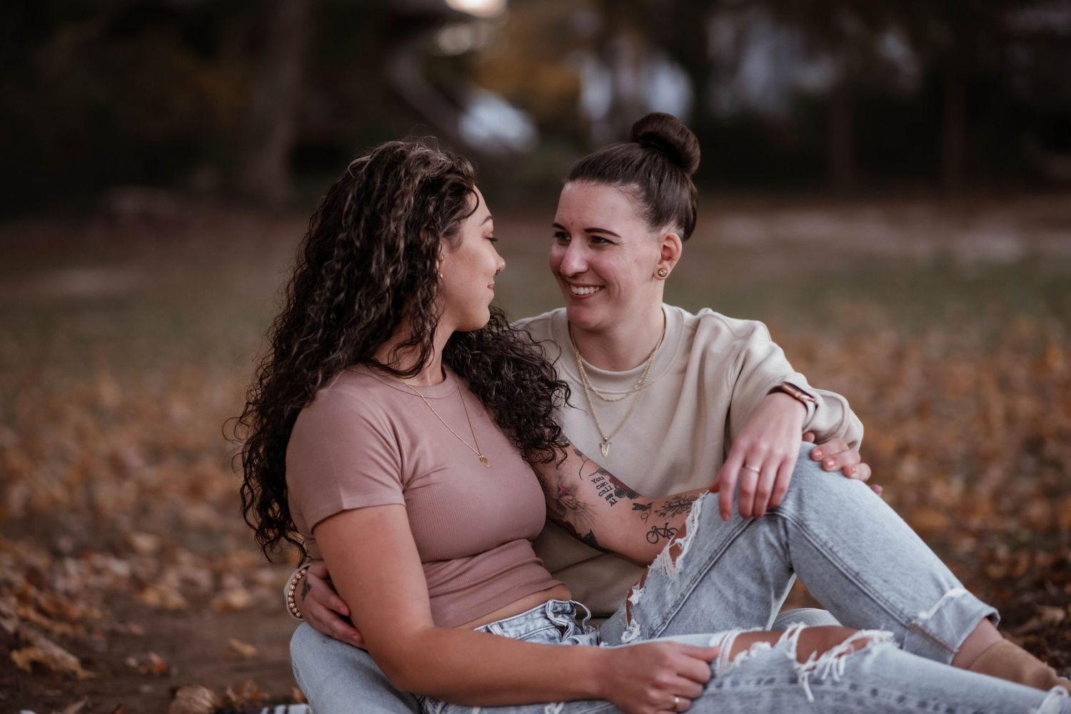 Young couple sitting together on fallen autumn leaves in a park during a romantic outdoor photoshoot.