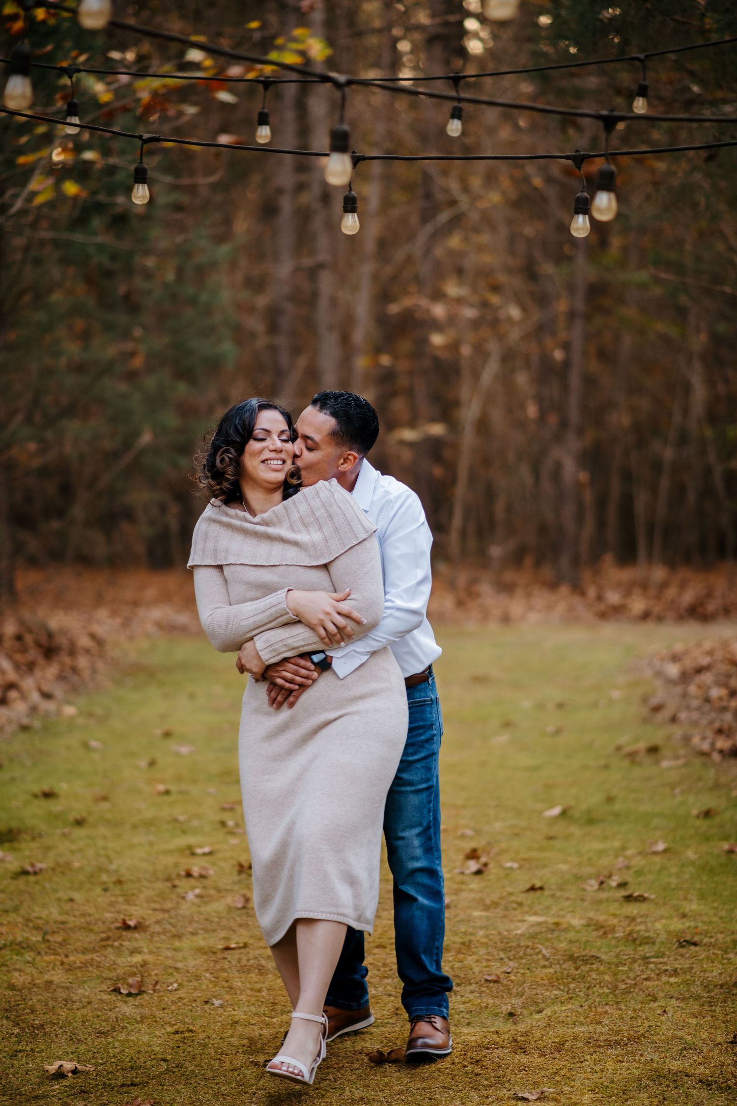 Couple sharing tender moments on grassy field with string lights overhead.
