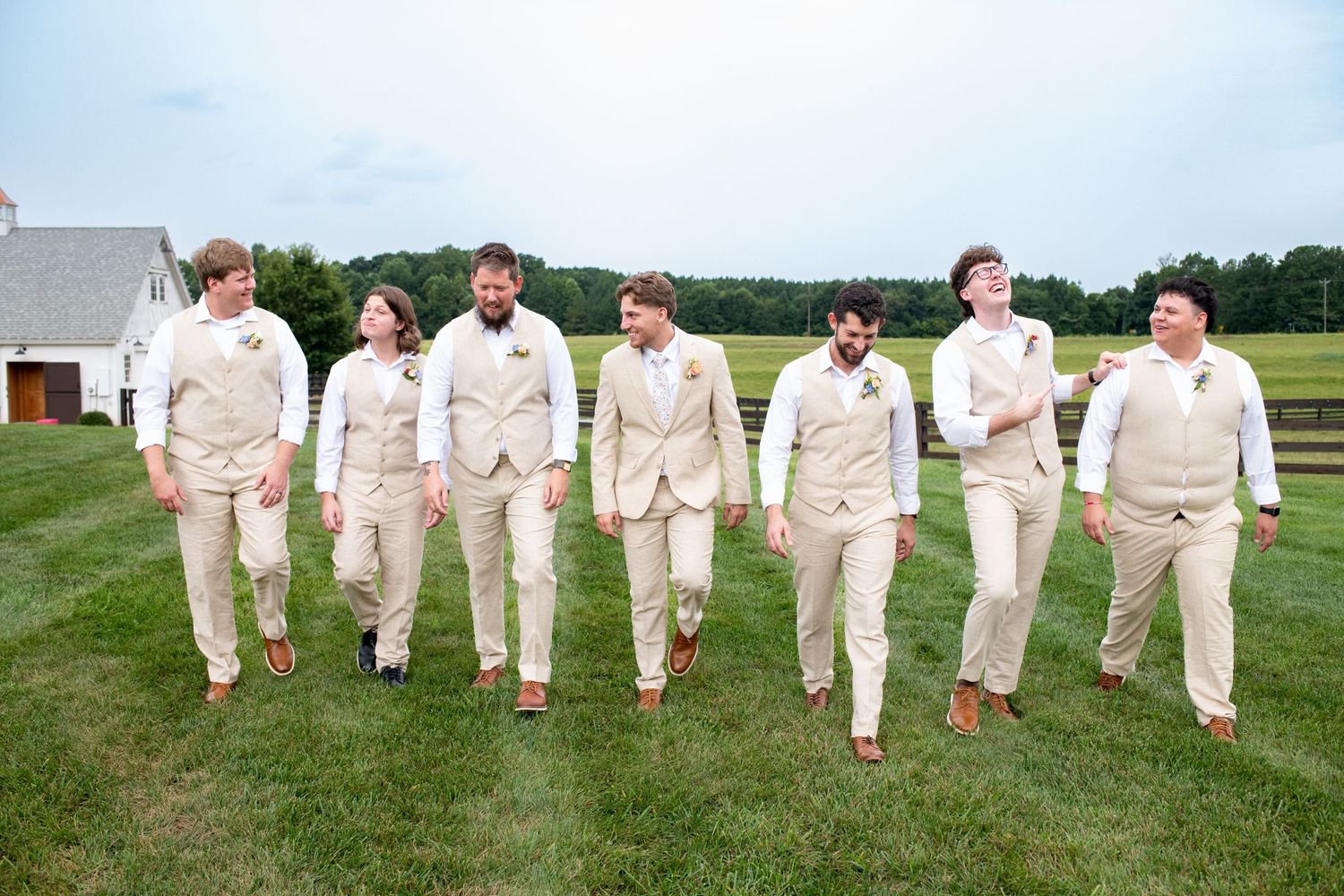 Groomsmen in beige suits walking together on grass outside.