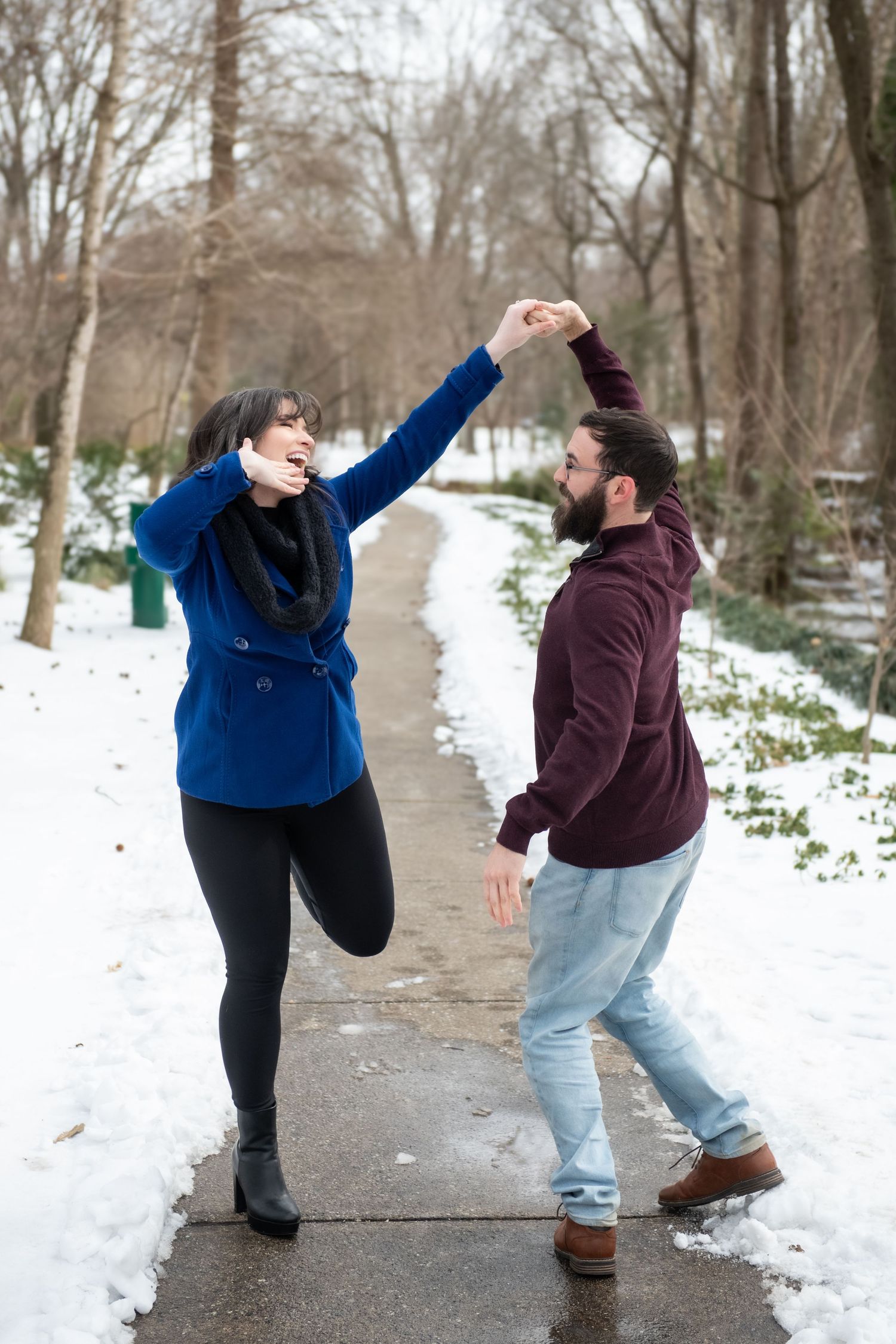 Two people strike dramatic dance poses on a snowy path during a winter photoshoot.