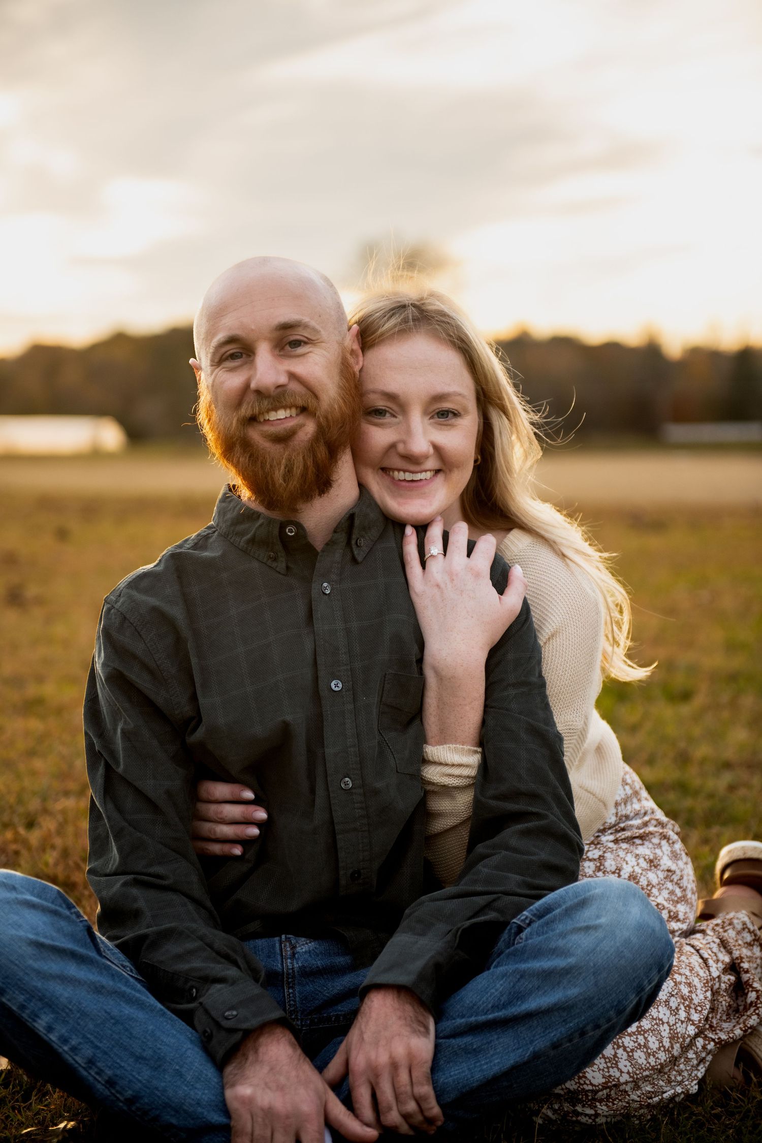 A couple shares intimate moments while sitting together in a sunlit meadow at sunset.