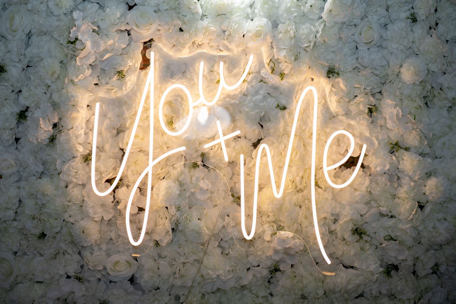 Neon sign reading You and Me on a white floral wall backdrop, perfect for weddings or romantic events.