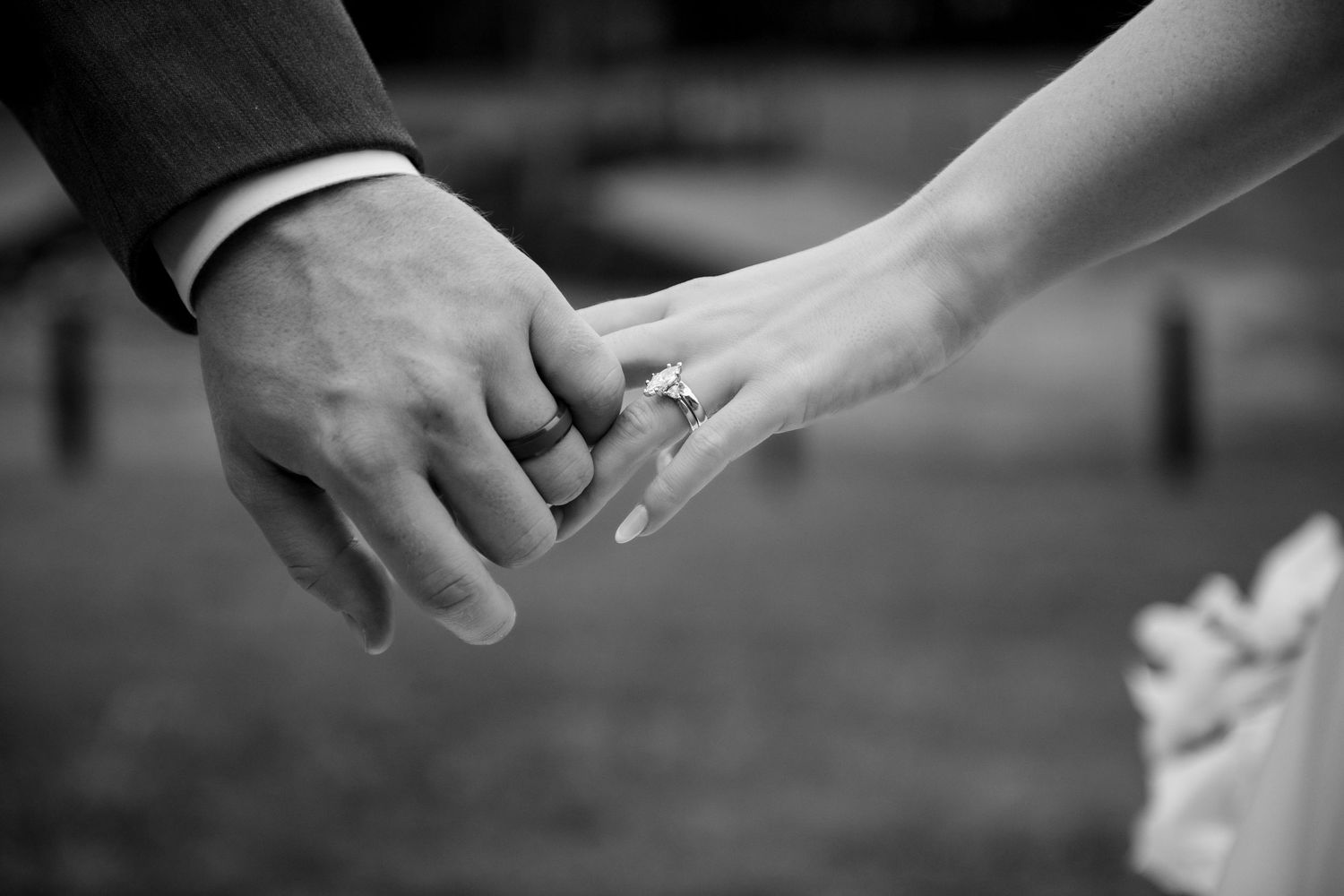 Black and white photo of a bride and groom holding hands, showcasing a sparkling diamond engagement ring.
