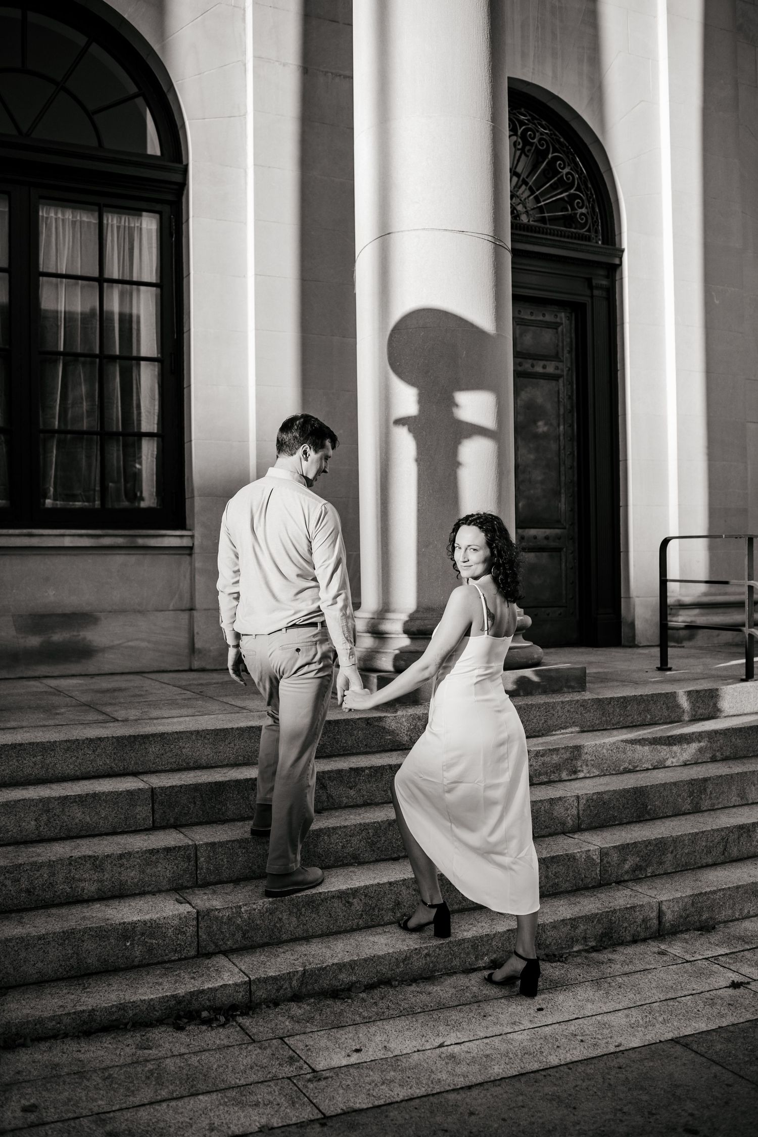 A couple ascending stone steps of a classical building in black and white.