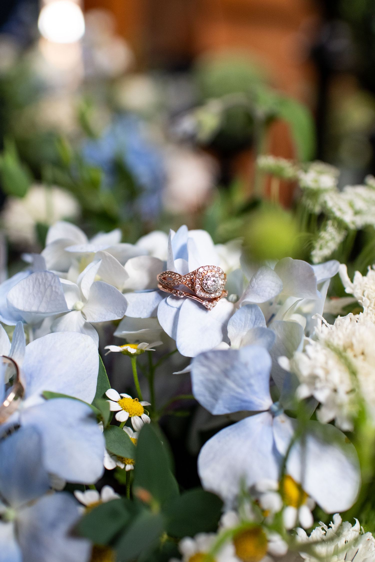 Wedding ring photographed among white hydrangeas and daisies in a floral arrangement.