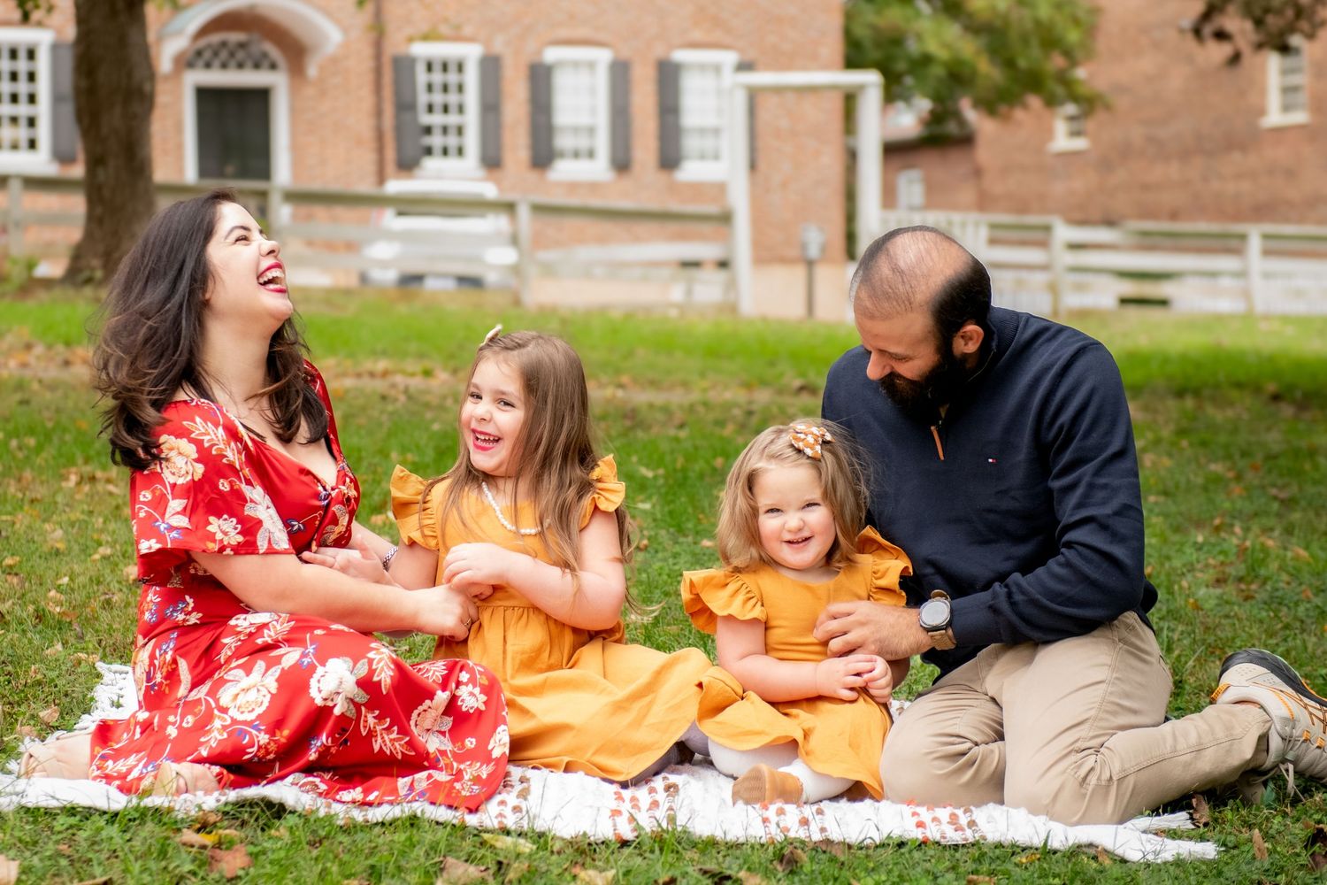 Family of four enjoying a fall picnic on a blanket outdoors, with two girls in yellow dresses and parents in festive attire.