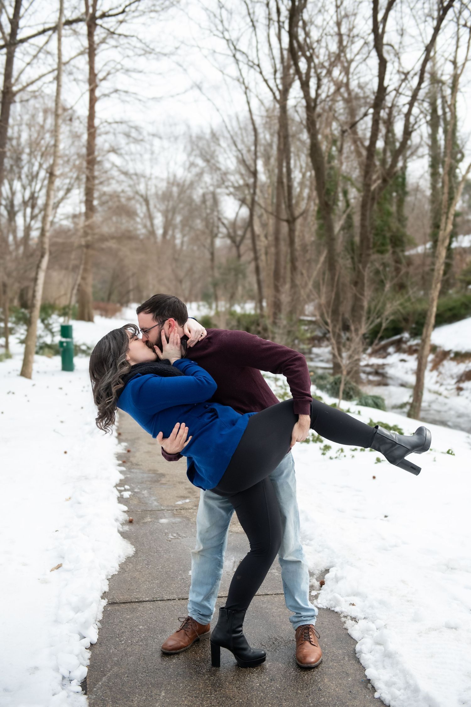 A couple performs a romantic dip pose while dancing together on a snowy winter path.