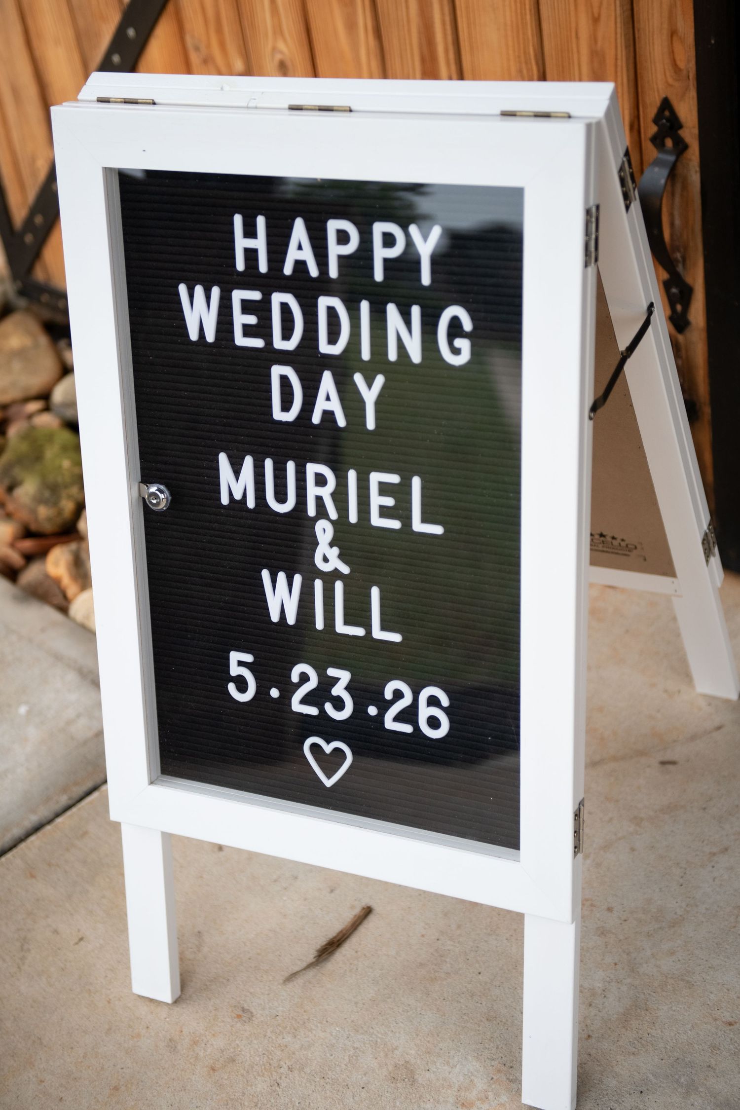 White A-frame letter board sign reading Happy Wedding Day Muriel & Will 5.23.26 with a heart symbol outdoors.