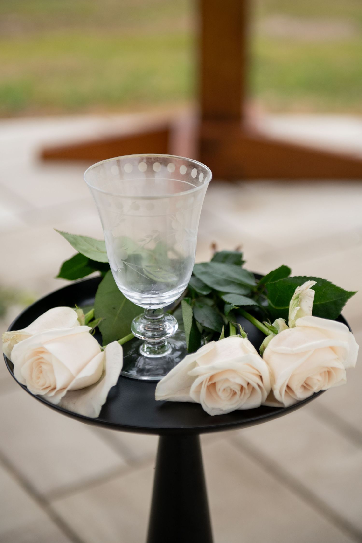 Elegant crystal wine glass surrounded by fresh white roses on a black pedestal table at a wedding ceremony.