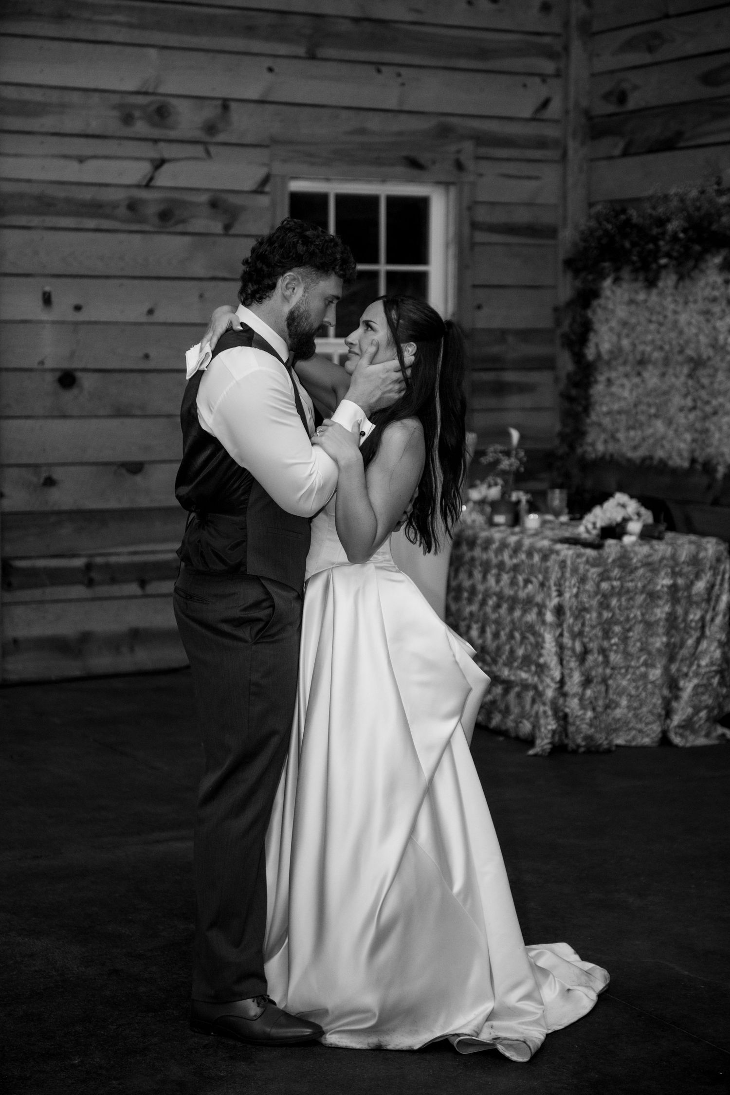 Black and white photo of bride and groom sharing an intimate first dance in a rustic barn wedding venue.