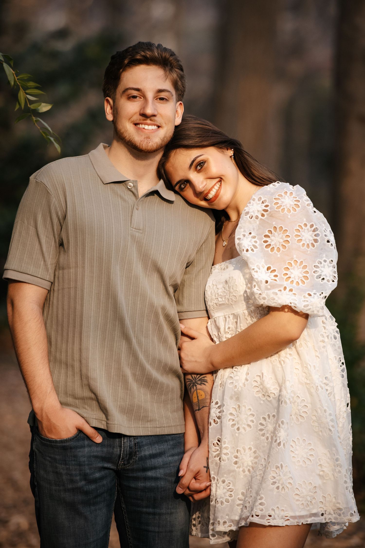 A couple in casual attire shares tender moments against a natural wooded backdrop.