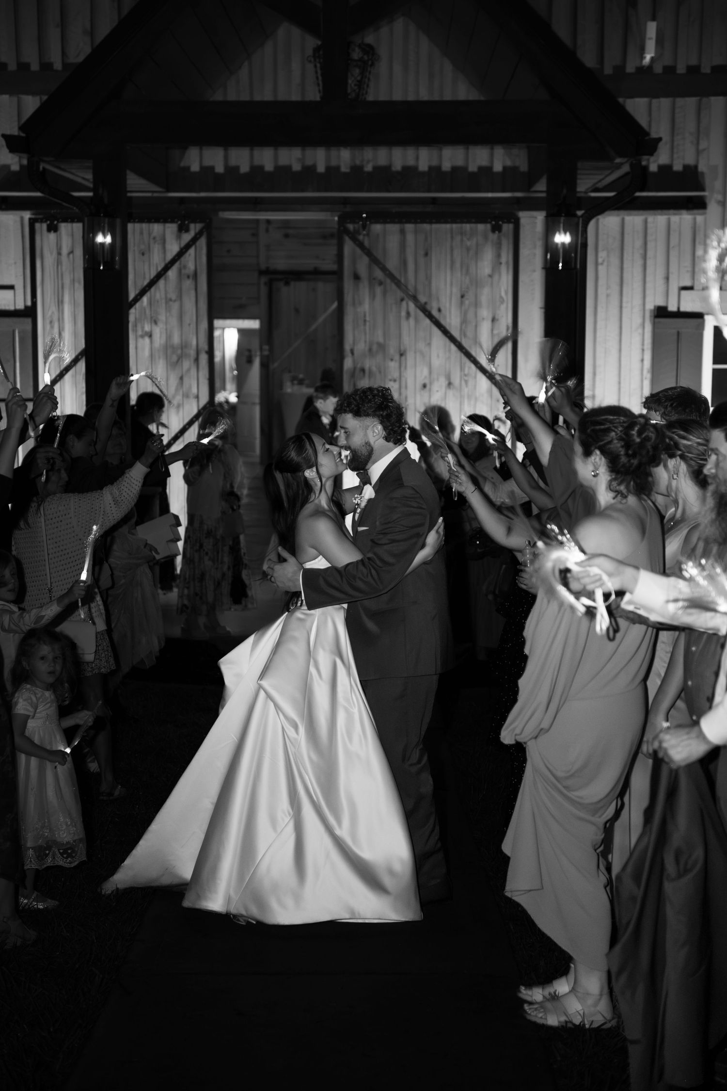 Black and white photo of a bride and groom sharing a kiss during their wedding exit with sparklers.