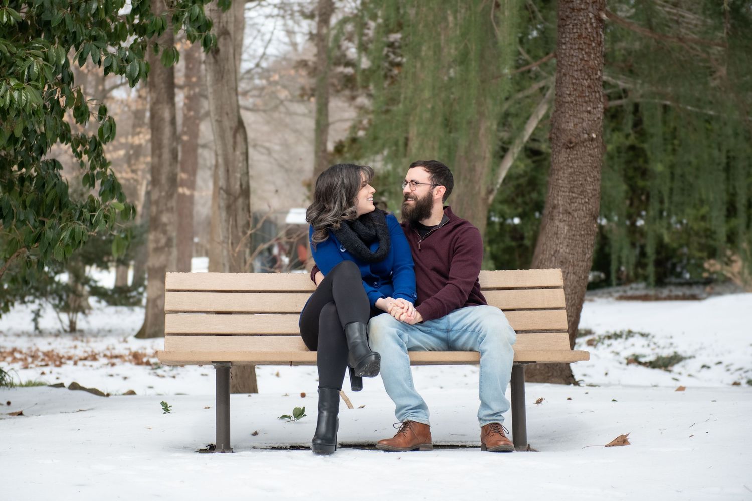 A couple shares a romantic moment lying in the snow during a winter engagement photo session in a snowy forest.