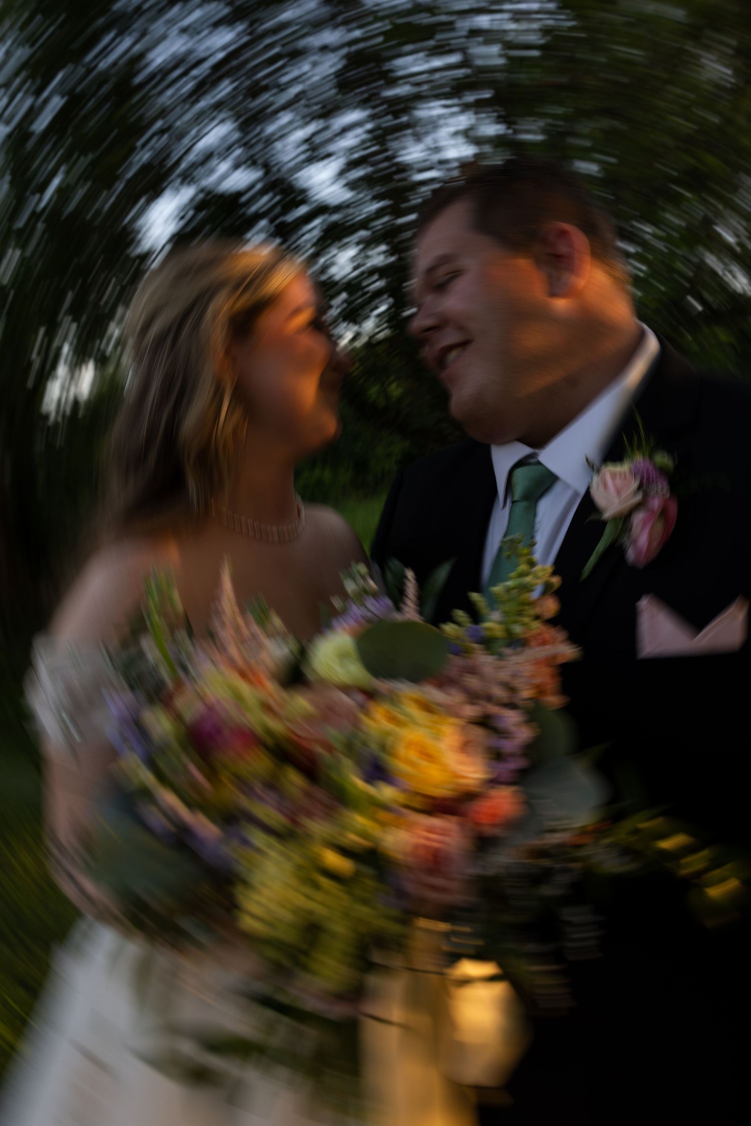 Bride and groom share a joyful moment with colorful bouquet, captured with artistic spin blur effect.