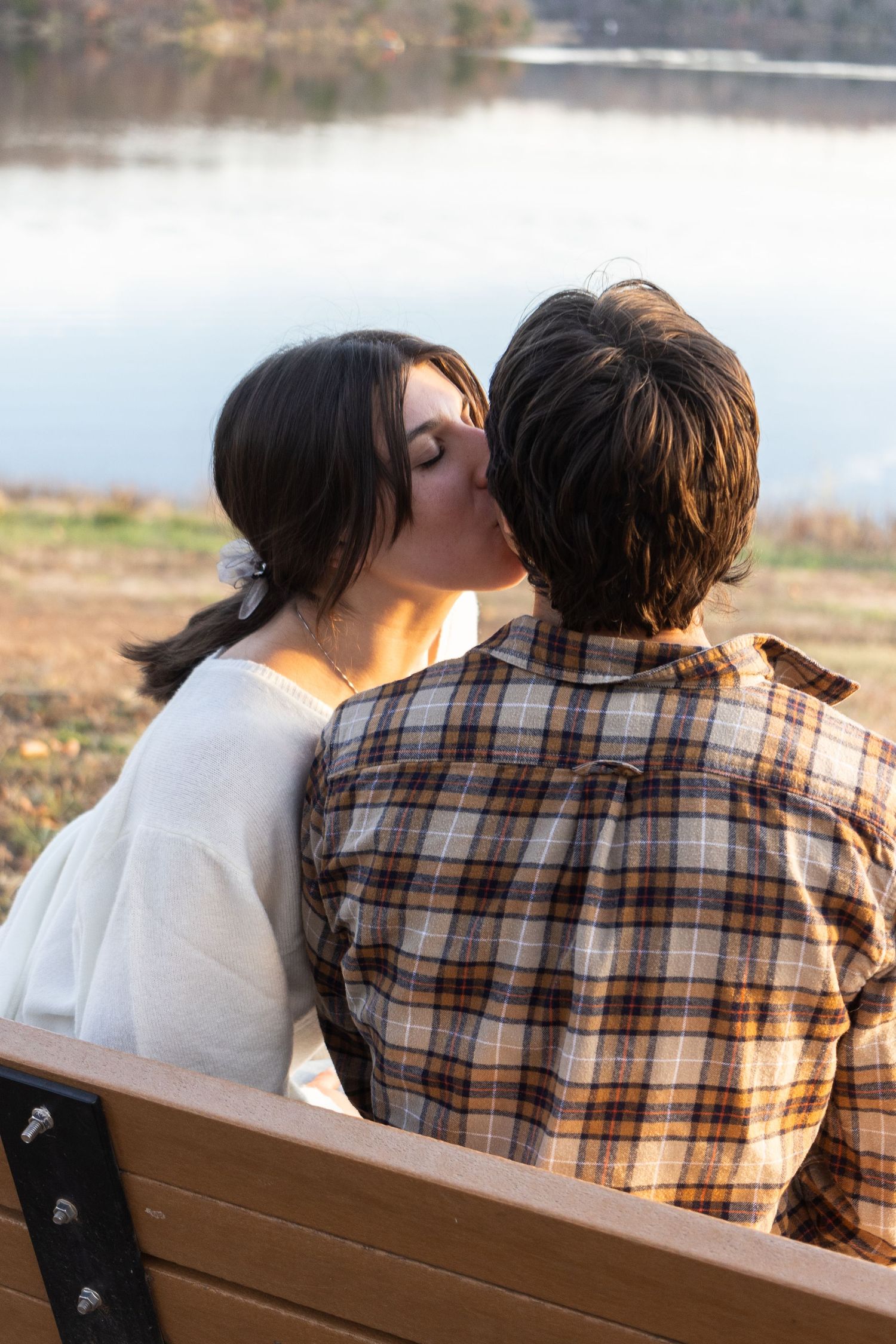 Romantic couple sharing an intimate moment on a bench by a lake at sunset.