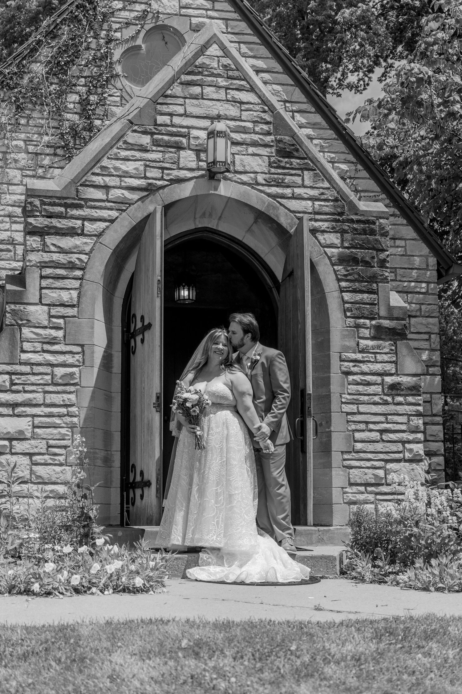 A couple shares an intimate moment in front of a stone church entrance with gothic arched doorways.