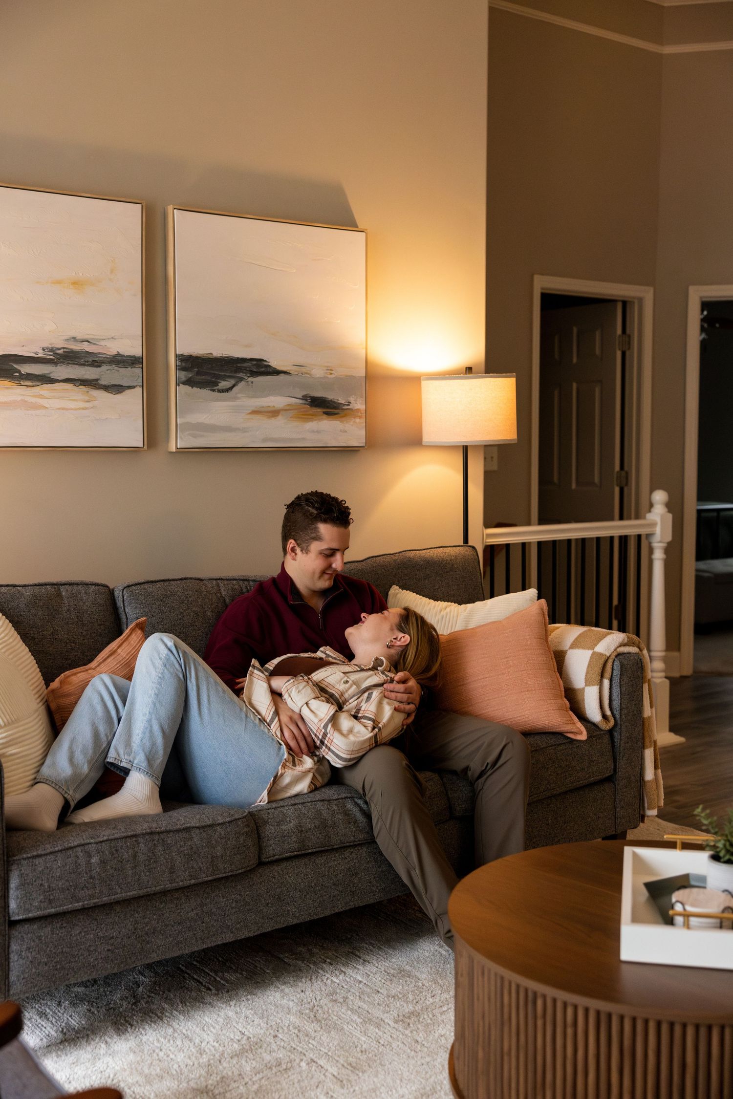 A couple relaxes together on a grey couch in a cozy living room with artwork.