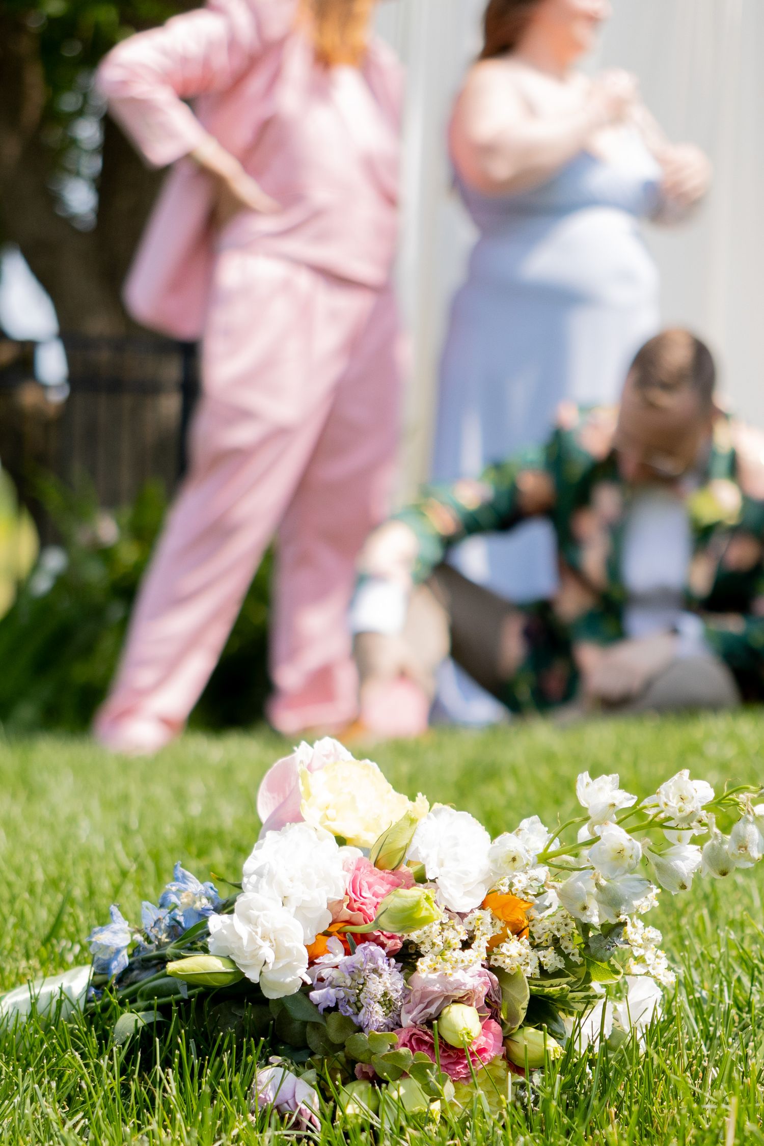 Colorful flower bouquets lay scattered on green grass with pink and white clothing visible in background.