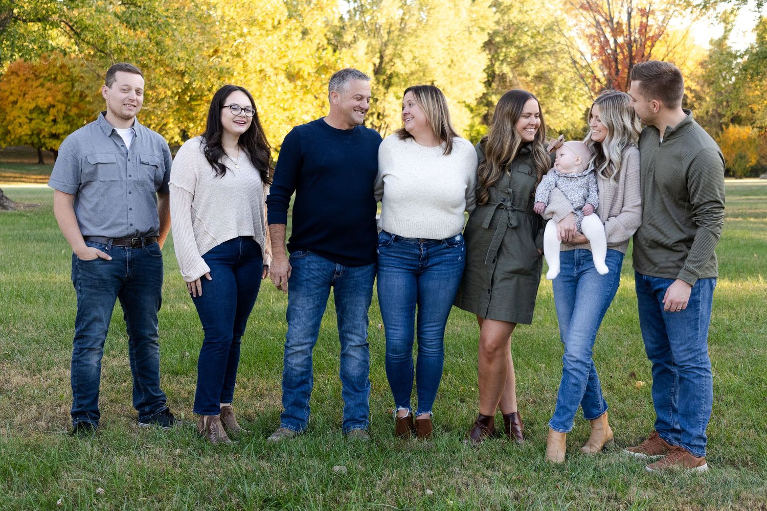 Large family group portrait with autumn trees and golden light in background.