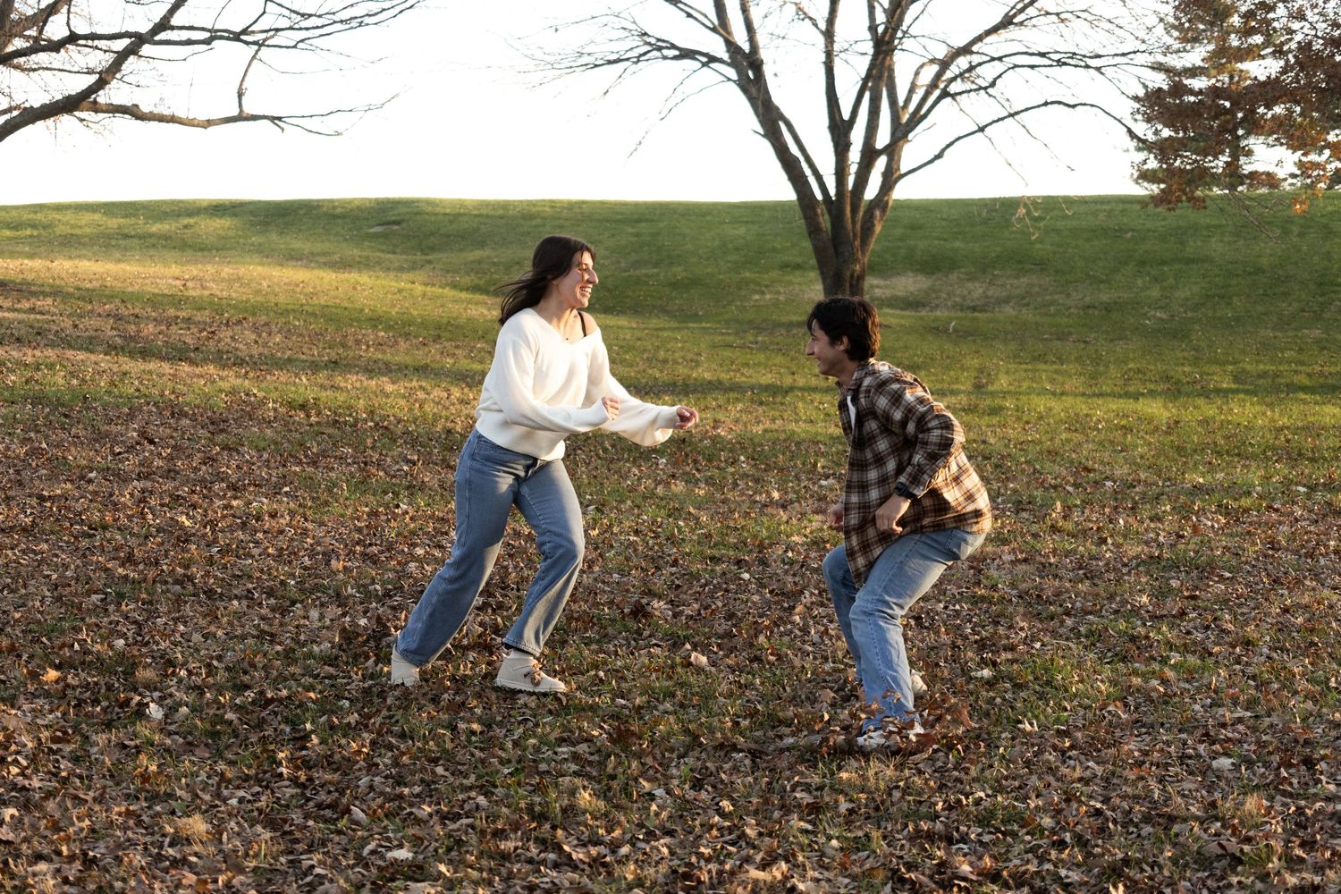 Playful couple in casual wear running through autumn leaves.