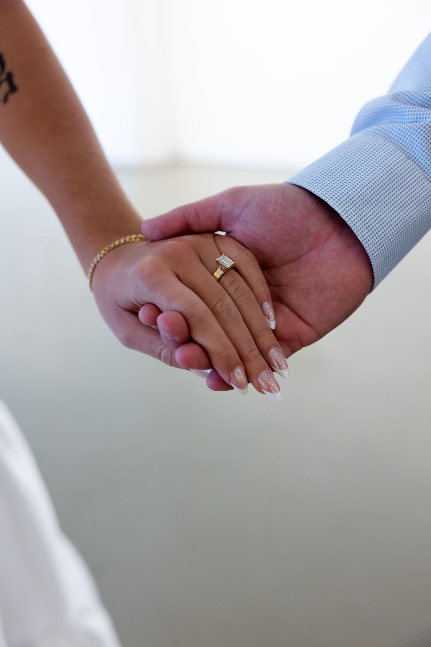 Close-up of couple holding hands, woman wearing gold engagement ring with French manicure and gold bracelet.
