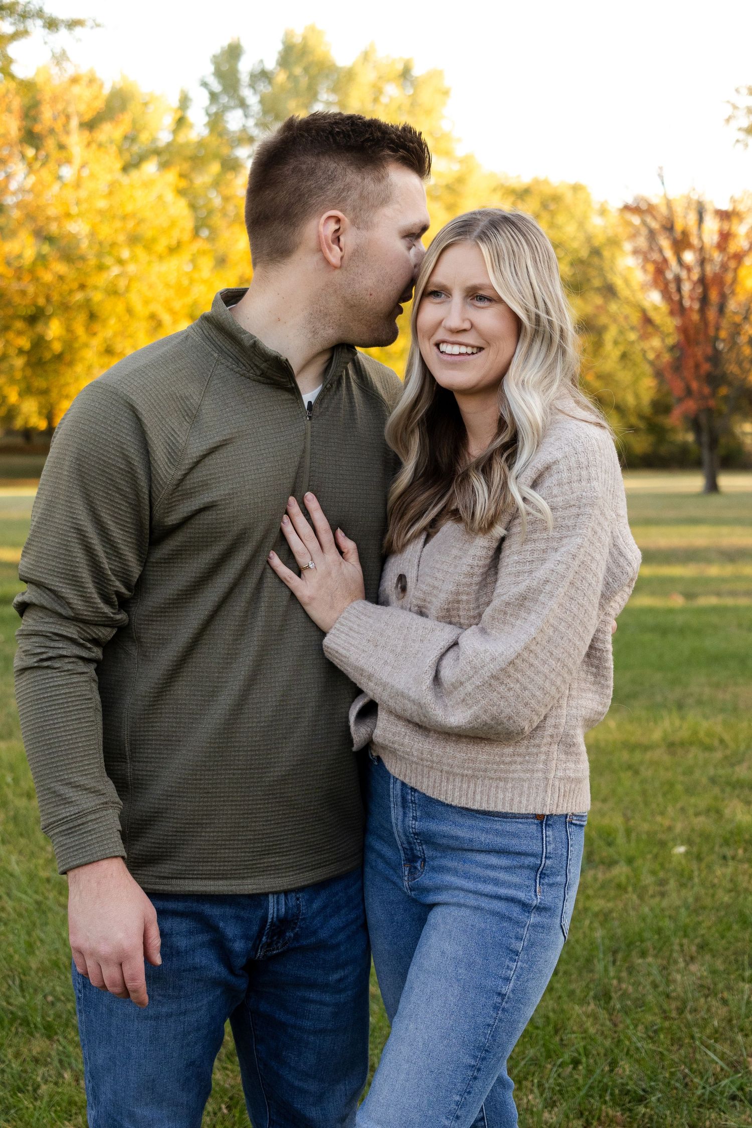 Couple shares an intimate moment while wearing cozy sweaters in a park during fall.