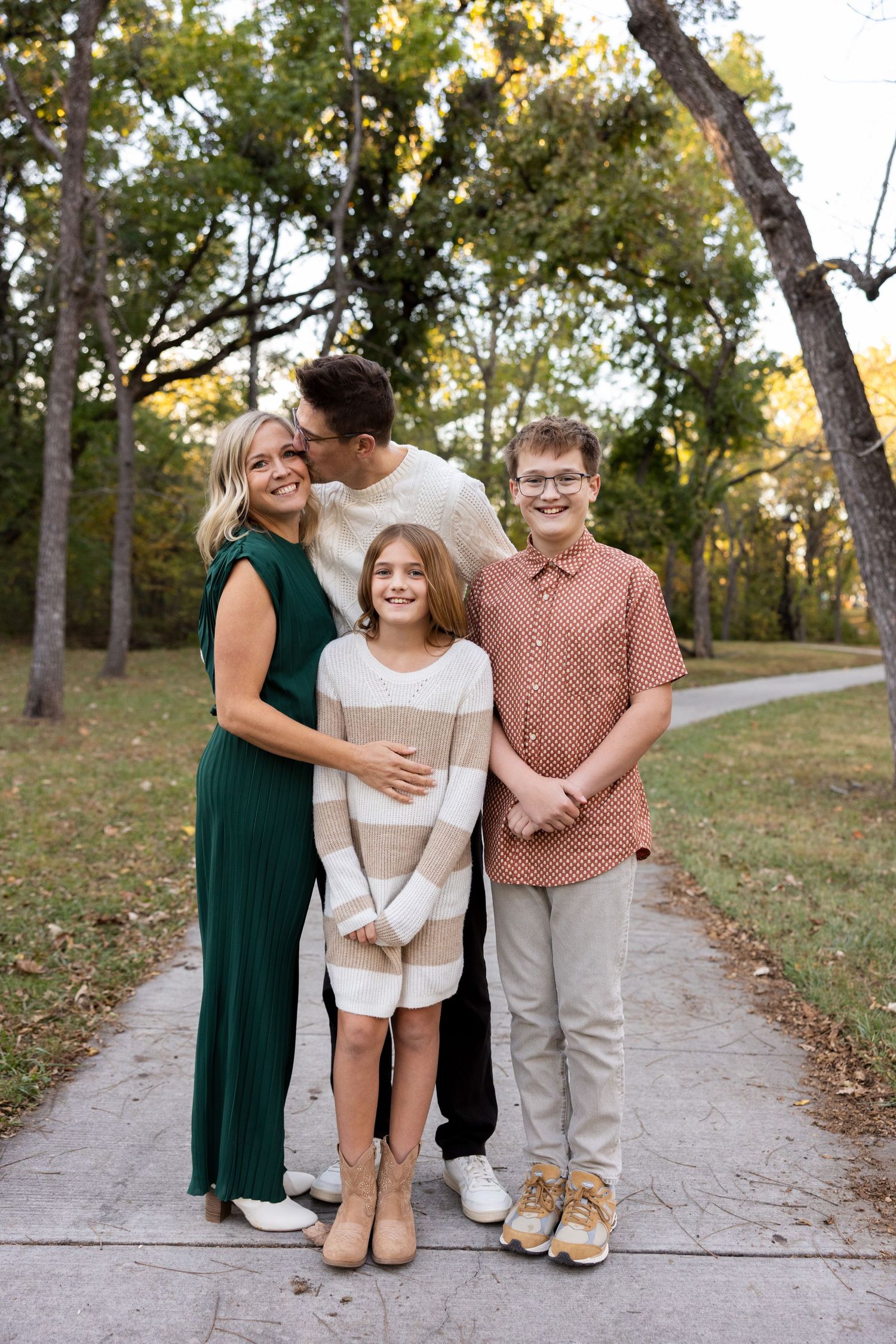 A family walks together on a paved path through an autumn park.