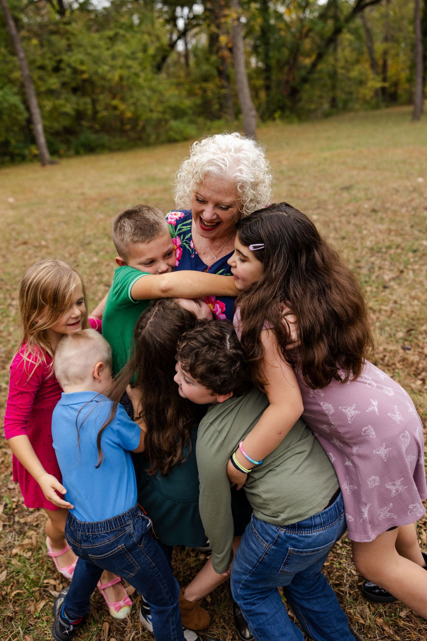 A joyful family group shares a warm embrace while playing outdoors in an autumn setting.