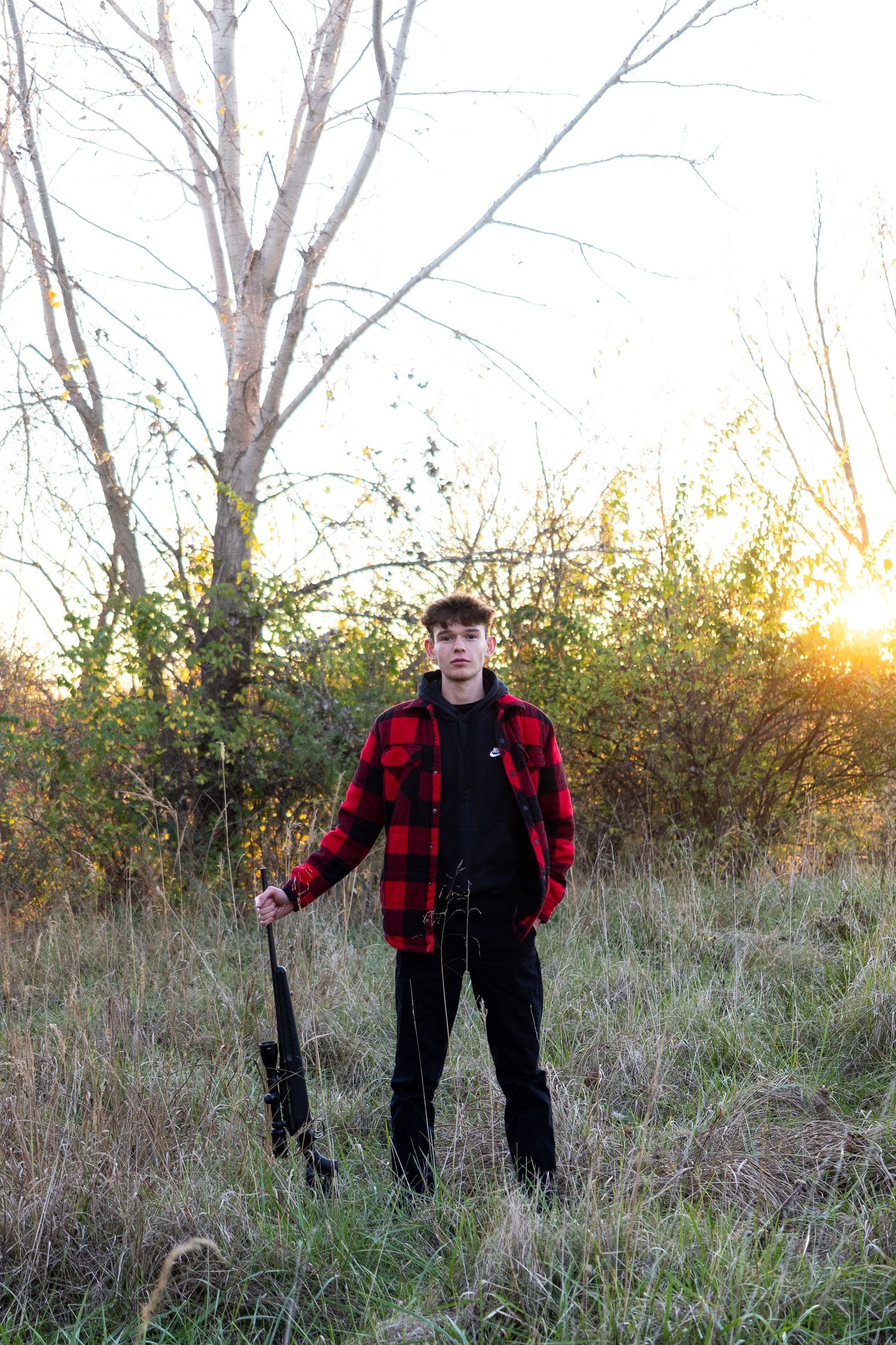 Person in red plaid jacket and black pants stands in autumn field at sunset.