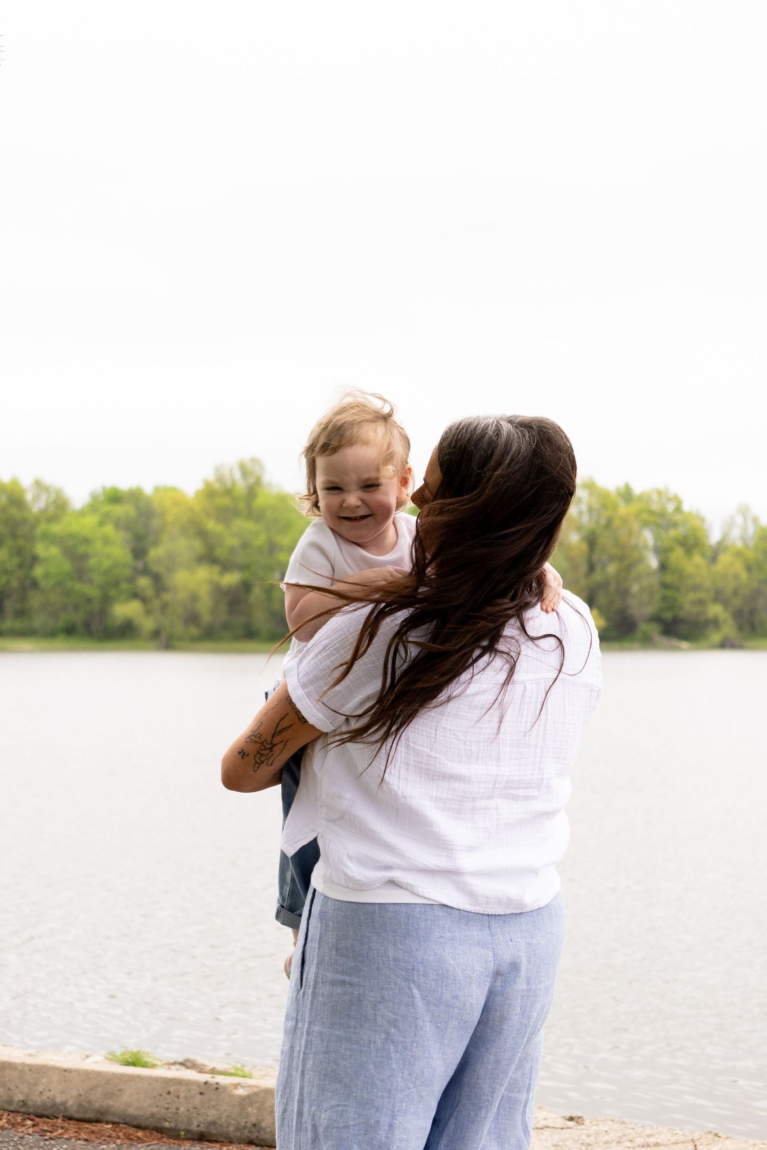 Mother and daughter share a tender moment while embracing by a serene lakeside on a sunny day.