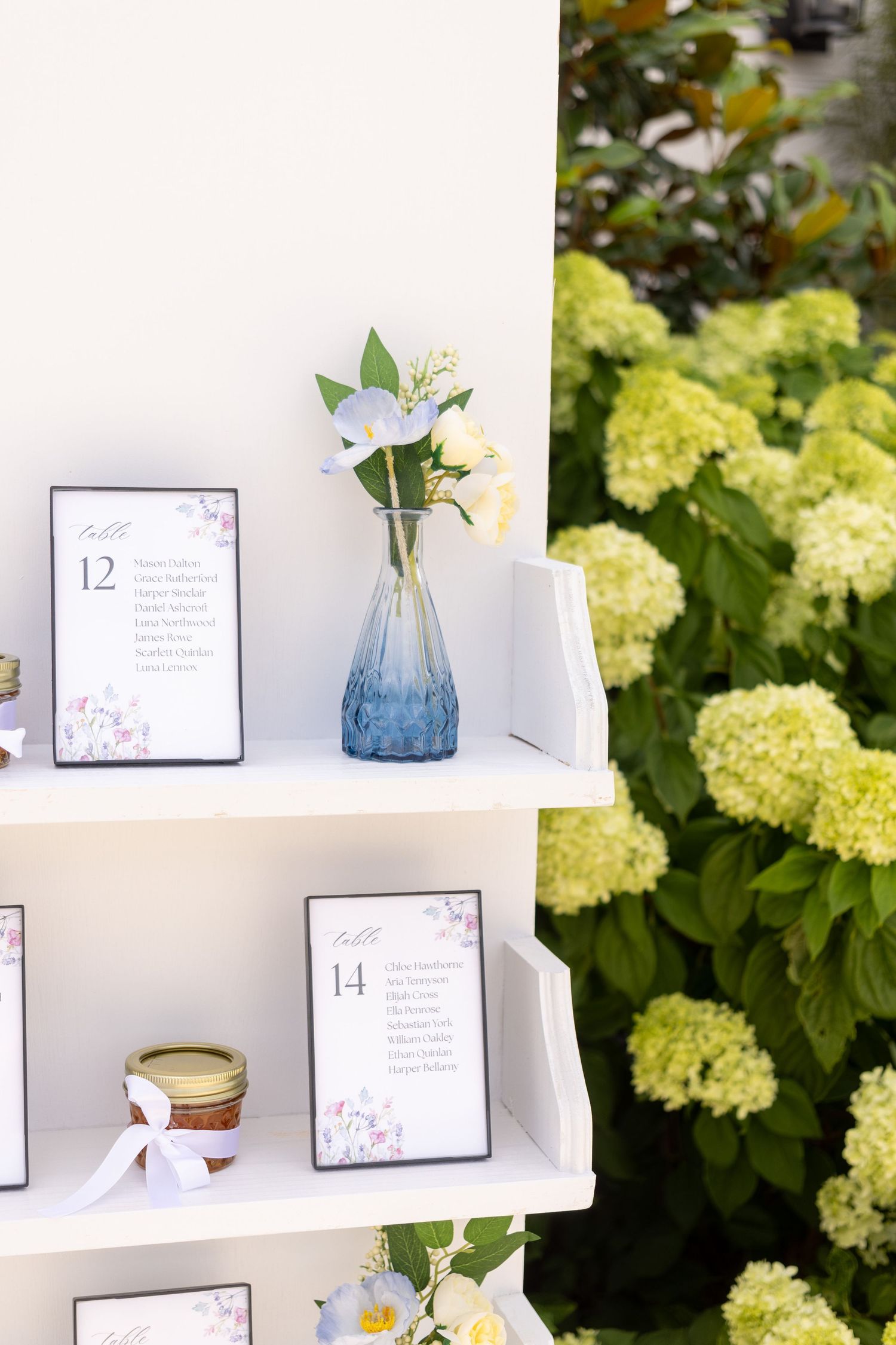 White shelves displaying wedding decor items with blue vases and yellow hydrangeas in the background.
