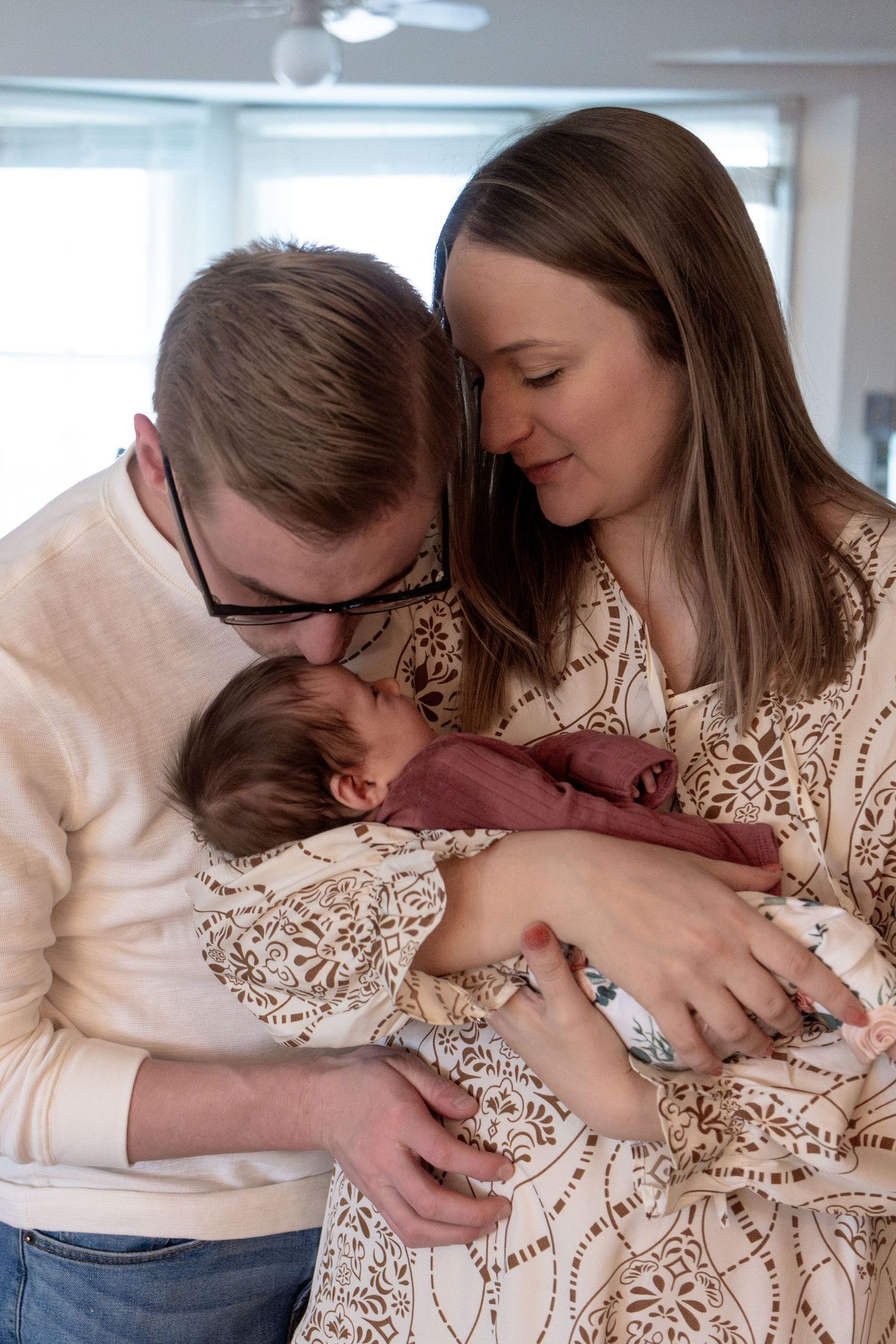 An intimate family portrait showing loving moments with a newborn in burgundy clothing.