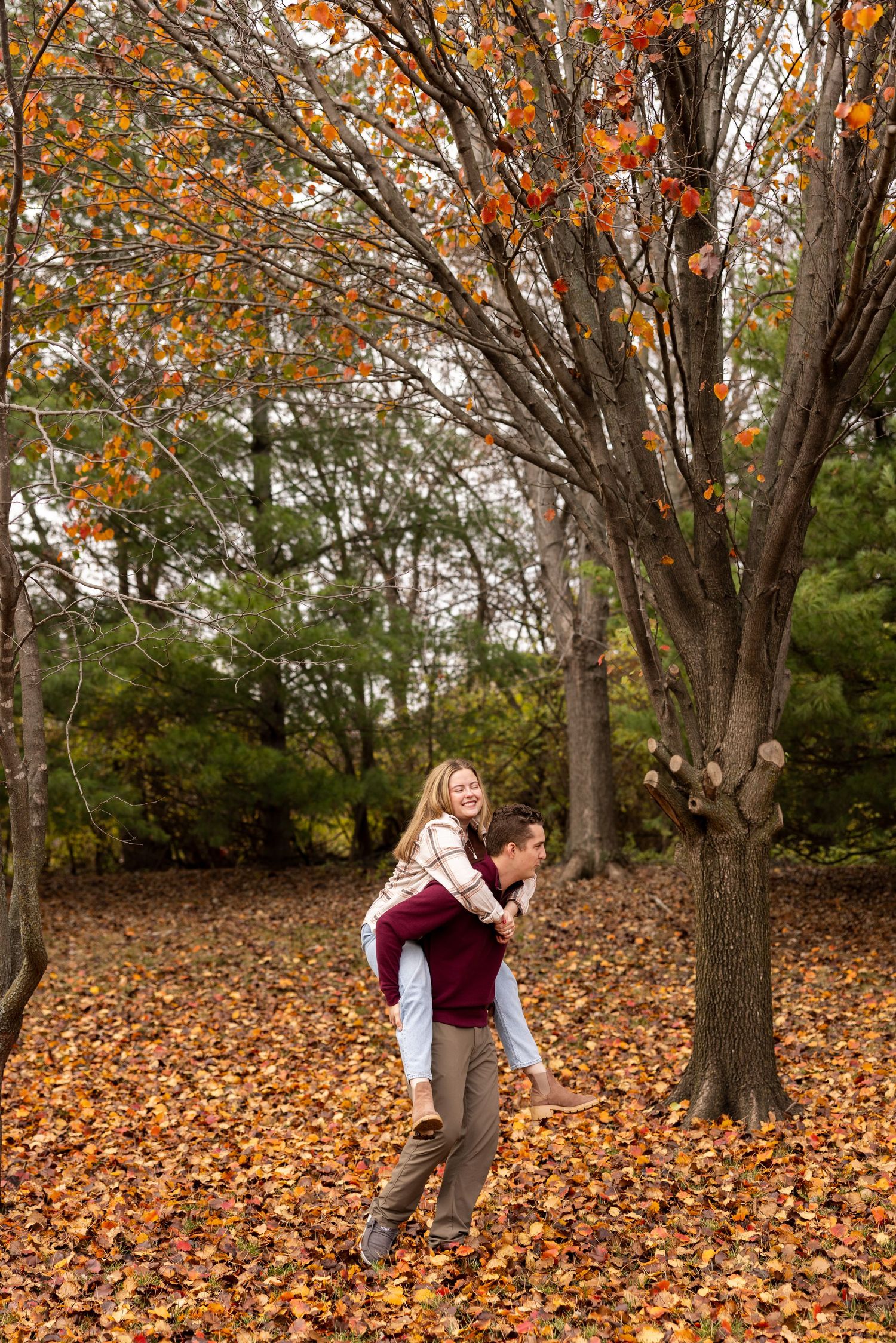 Two people play and laugh in a park covered with vibrant fall foliage.