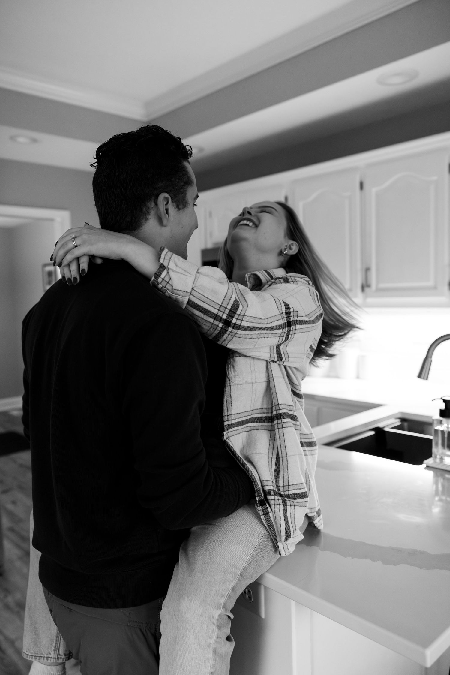 A couple dances together in a modern kitchen with white cabinets and warm lighting.